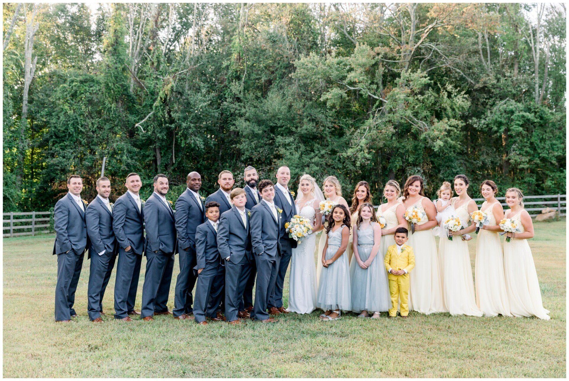 Wedding party posing outdoors in navy suits and cream dresses with a forest backdrop