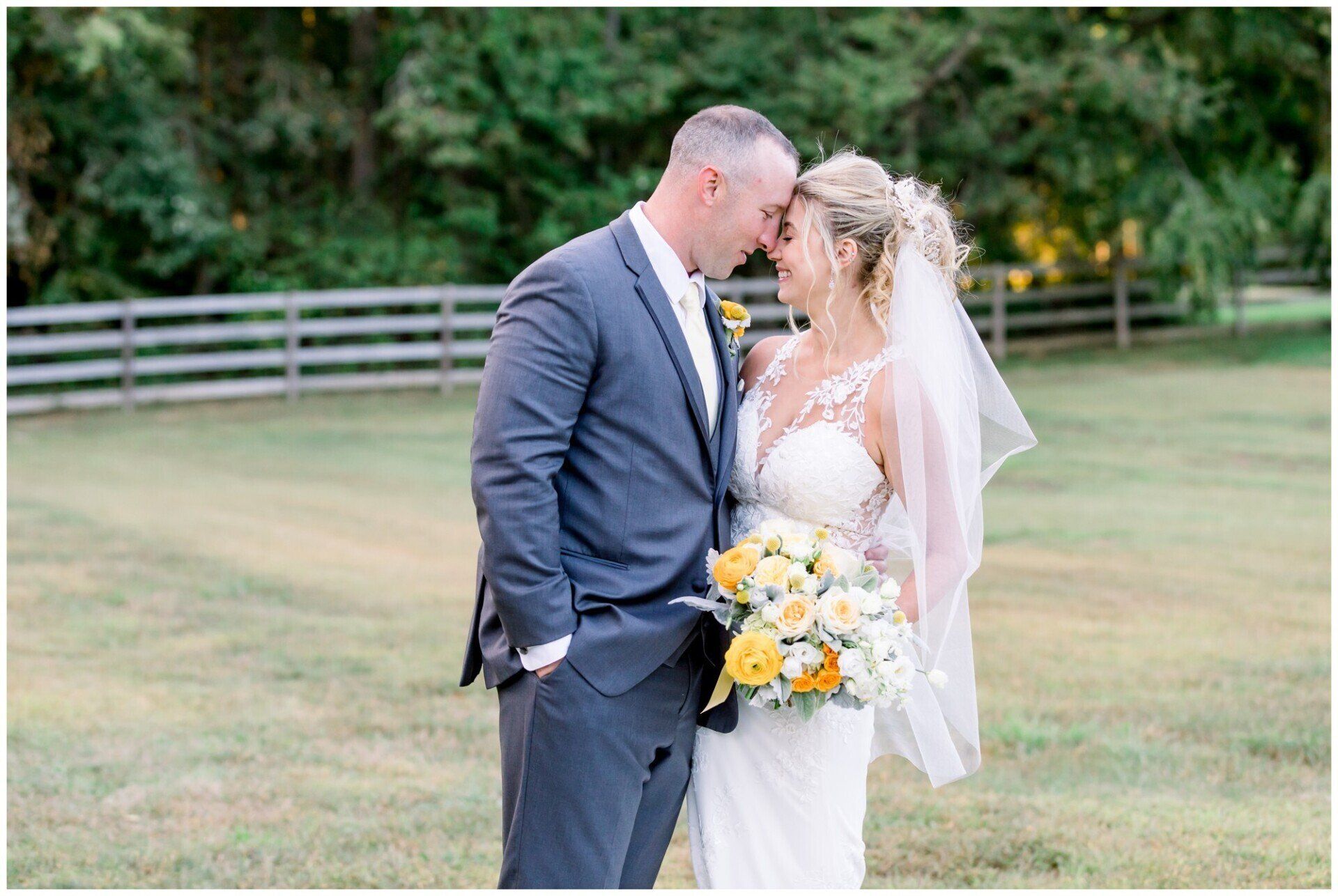 Bride and groom kissing outdoors in a grassy field, bride holding a yellow-and-white bouquet