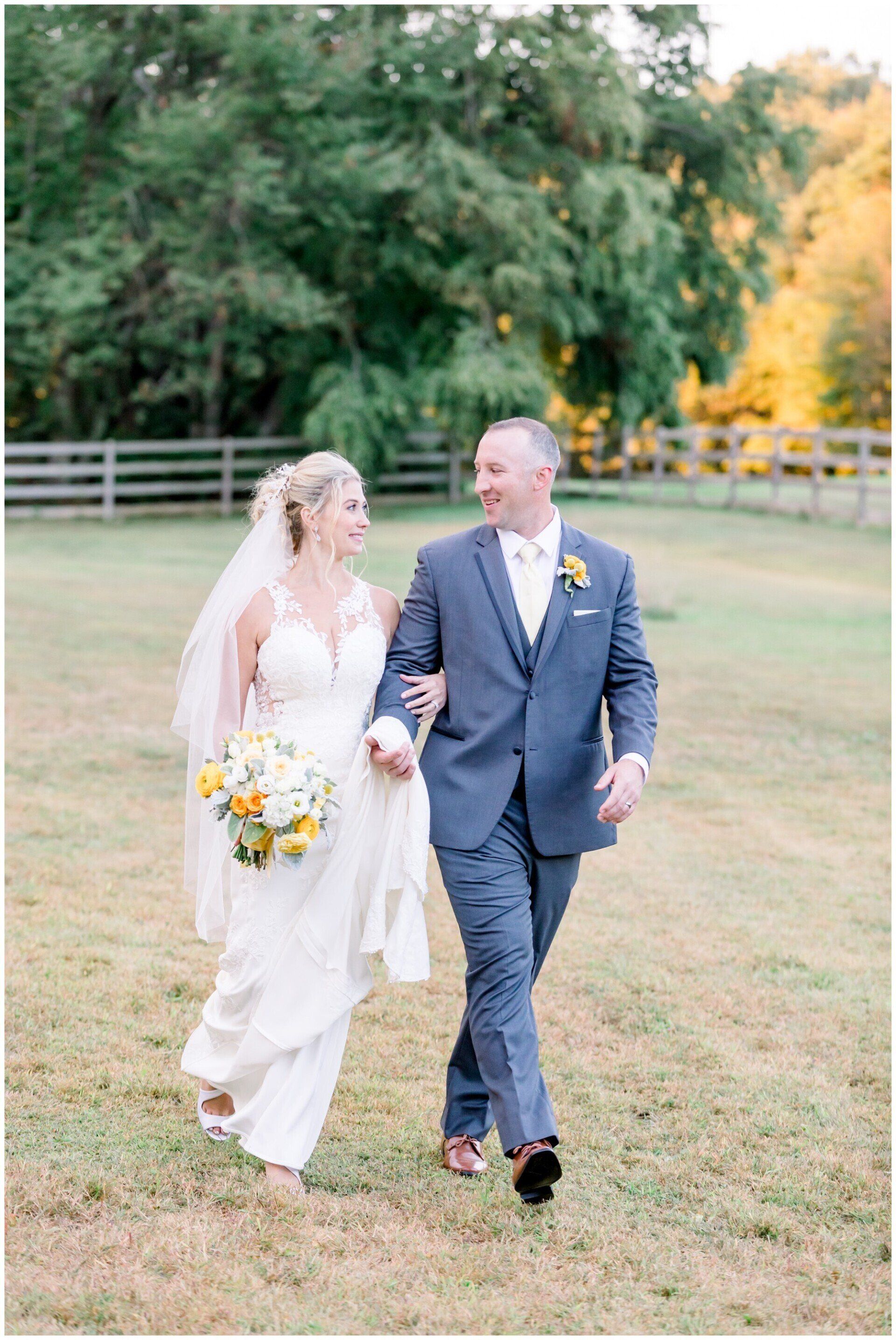 Bride and groom walking hand in hand on a grassy lawn with trees in the background
