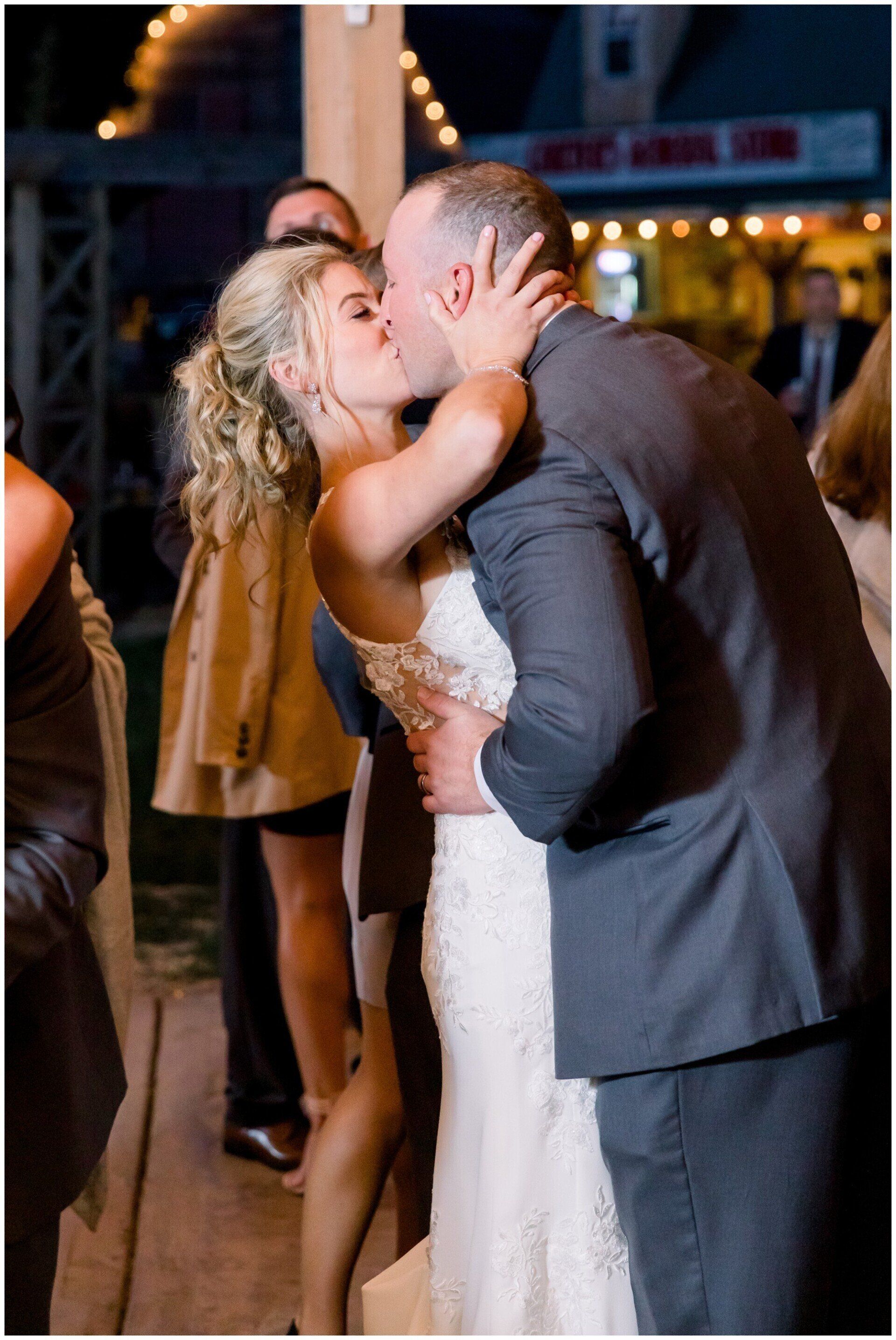 Bride in a white dress kissing a man in a dark suit at a nighttime celebration
