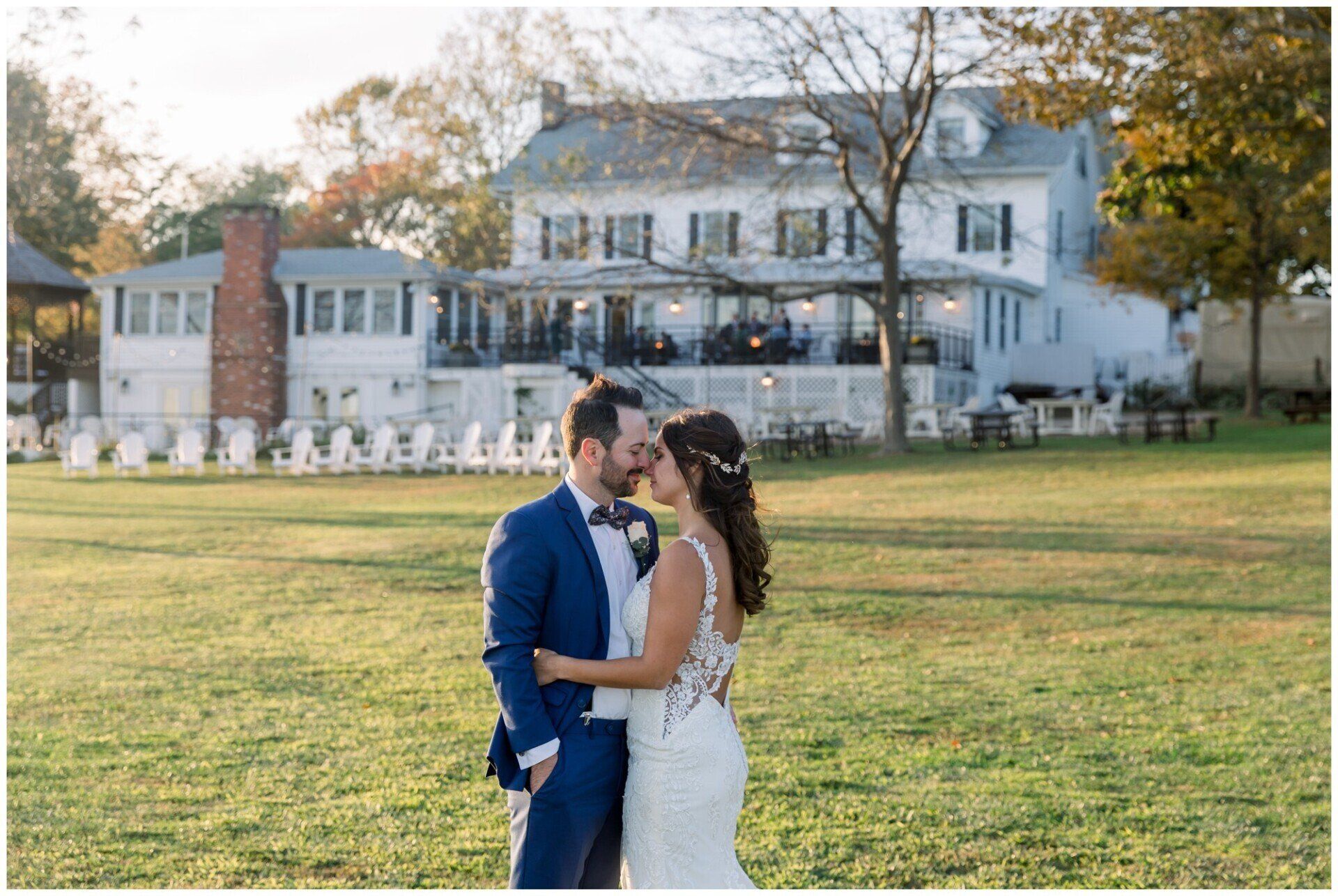 Bride and groom embracing on a lawn in front of a white house at sunset