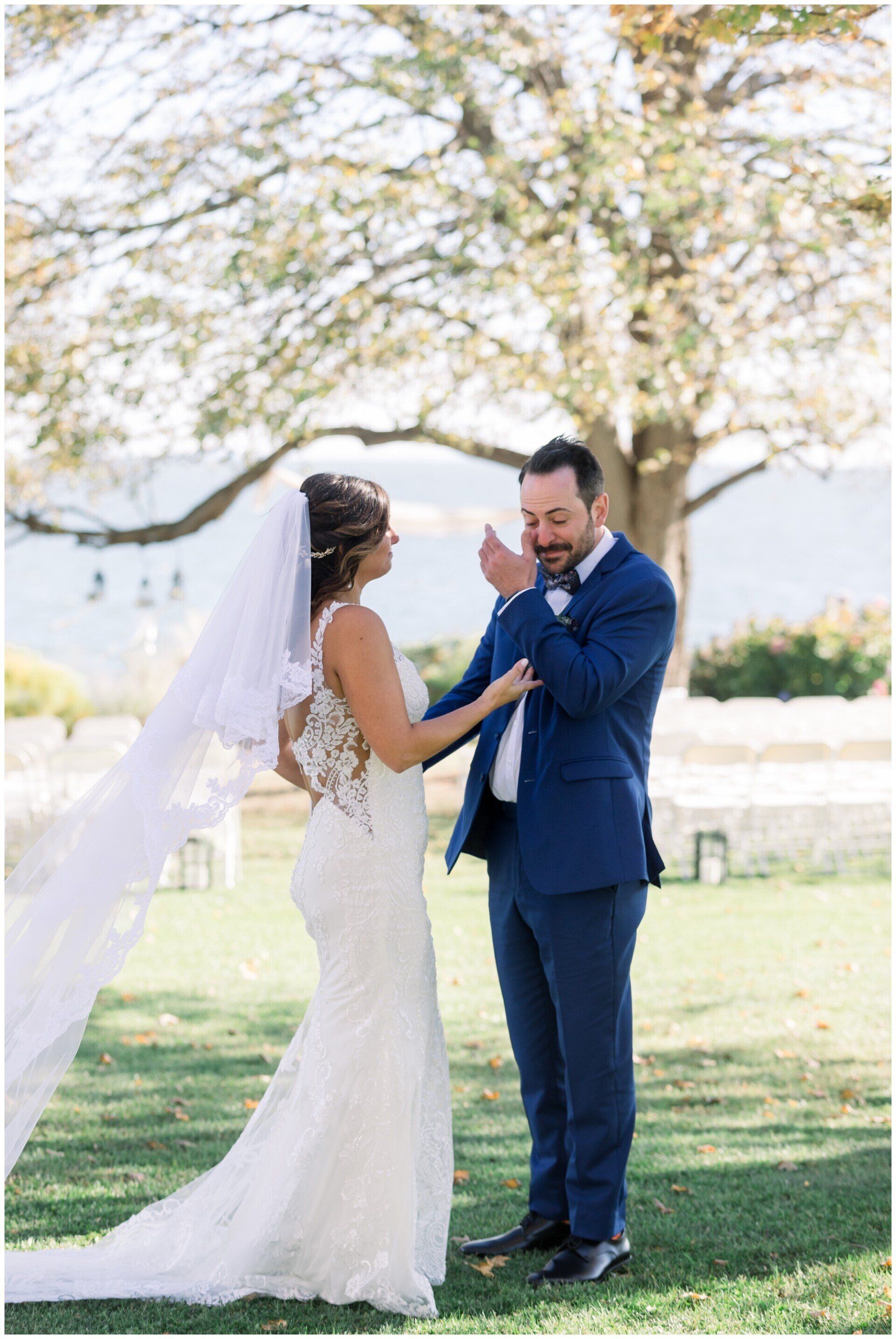 Bride and groom holding hands outdoors under a tree, smiling in wedding attire.