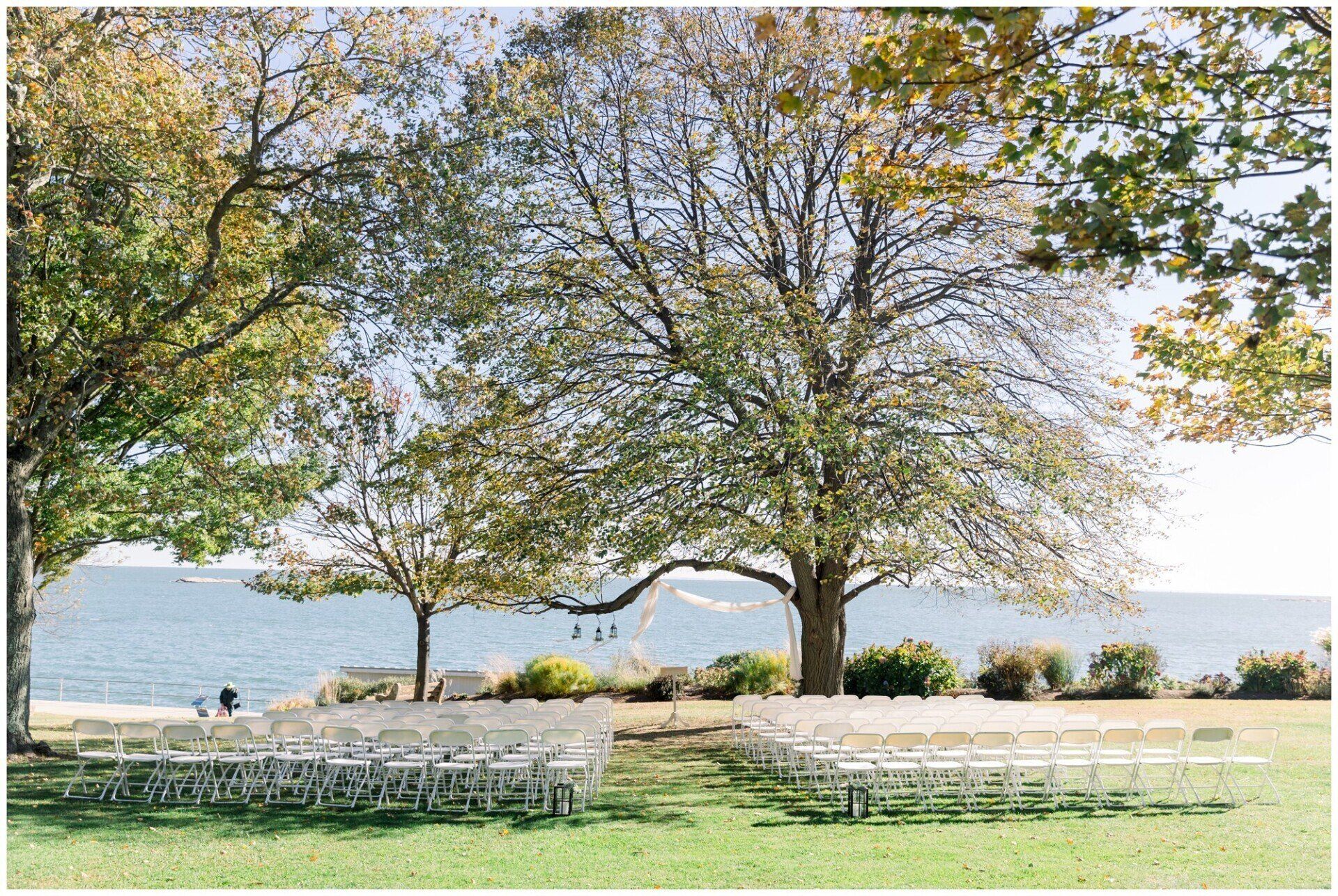 Park by a lake with trees and rows of white chairs under a bright sky