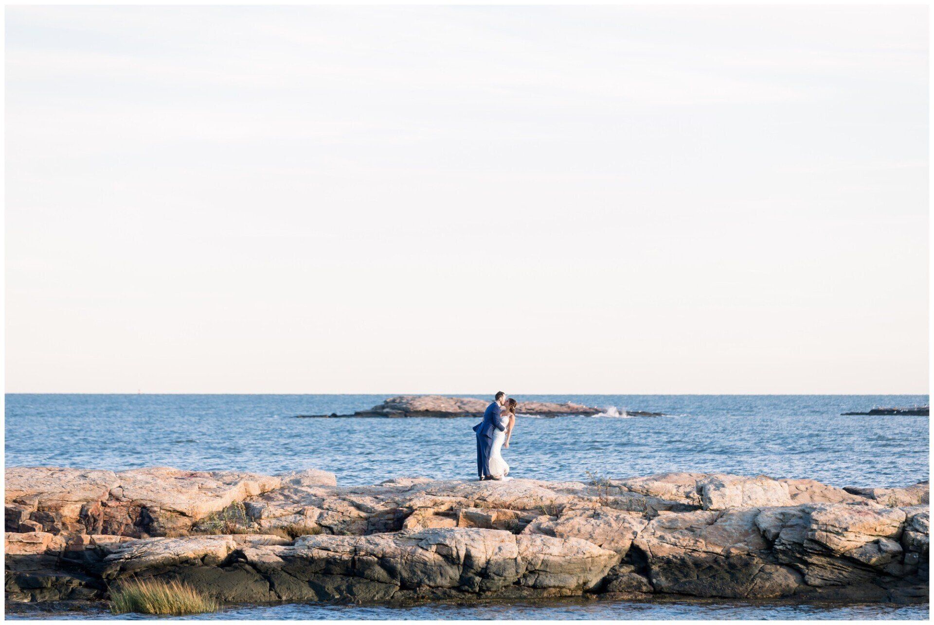 Person standing on rocky shore by the ocean under a pale sky