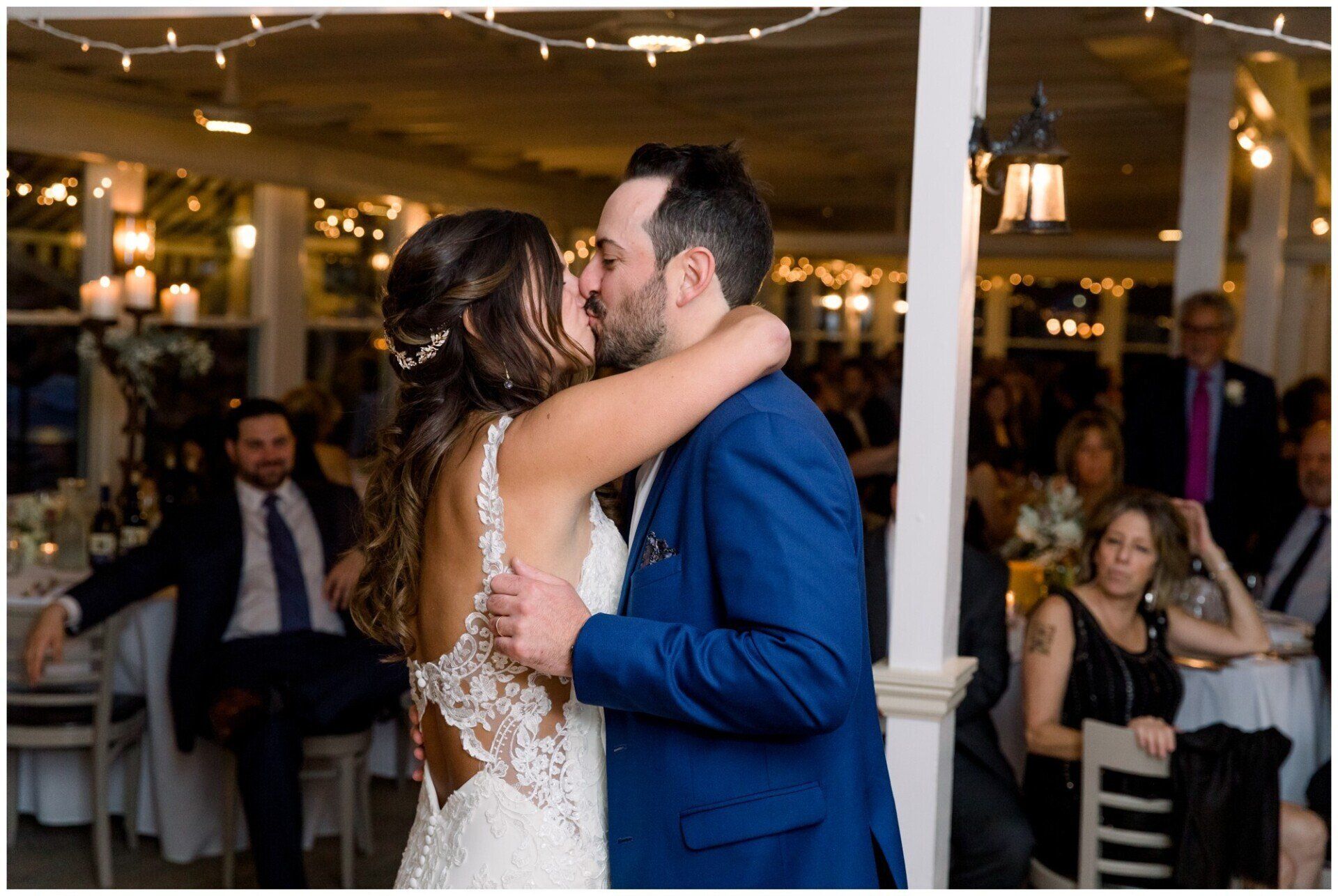 Bride and groom kissing at an indoor wedding reception, bride in lace dress and groom in blue suit