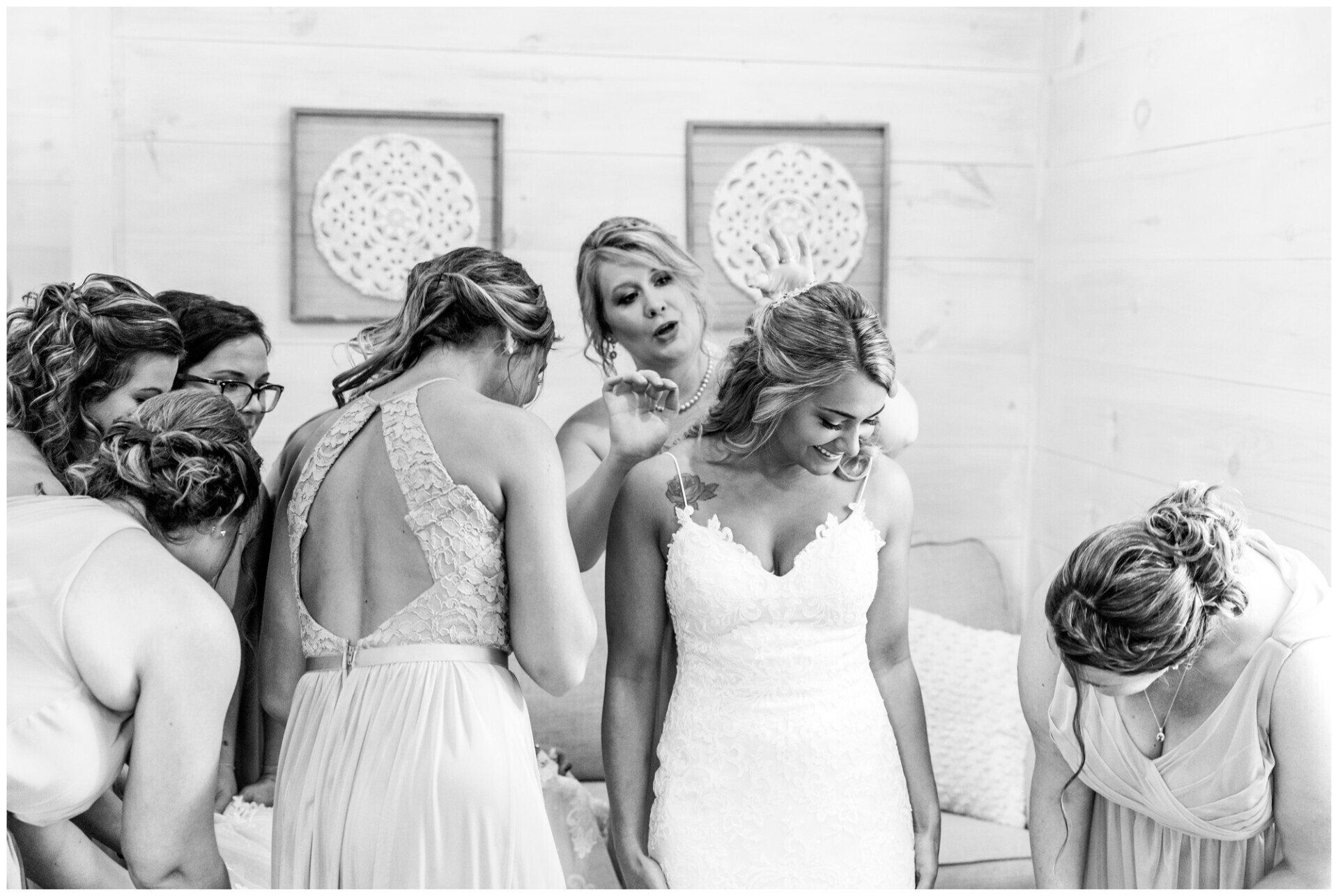 Bride and bridesmaids in white dresses getting ready, with one woman being fastened in the center