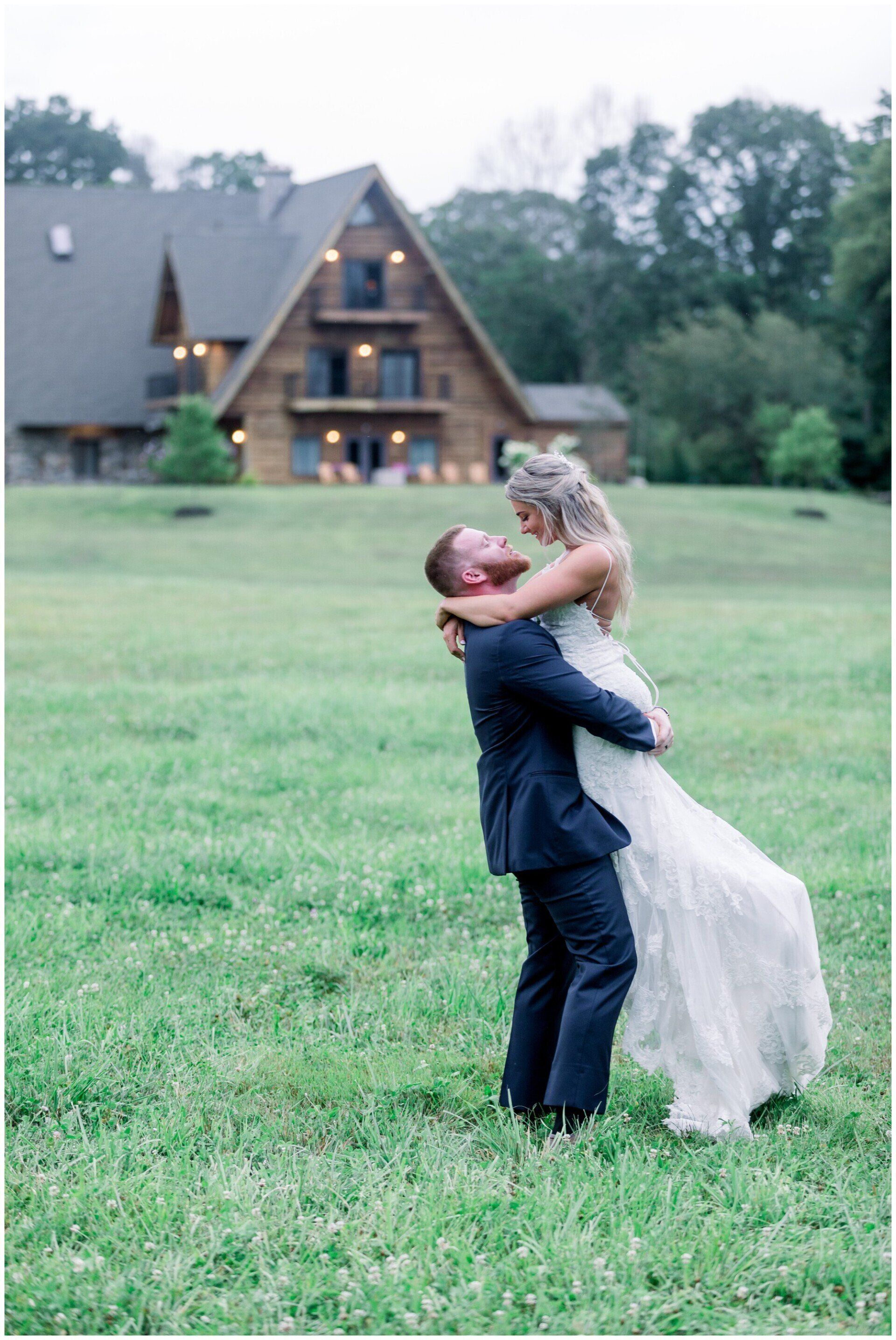 Couple embracing on a grassy lawn in front of a large A-frame house at dusk