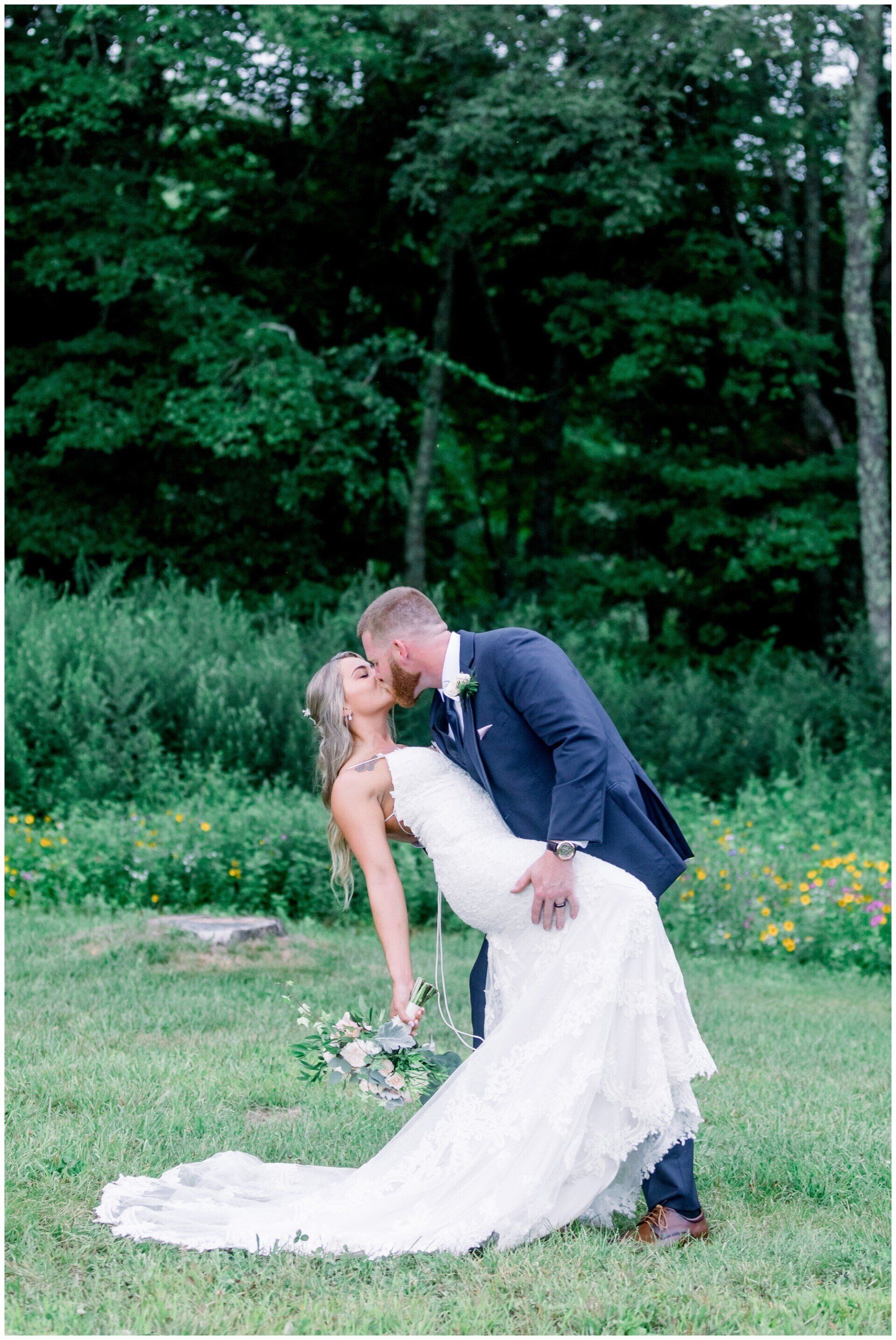 Couple kissing outdoors in a garden, with the bride in a white dress and the groom in a navy suit.