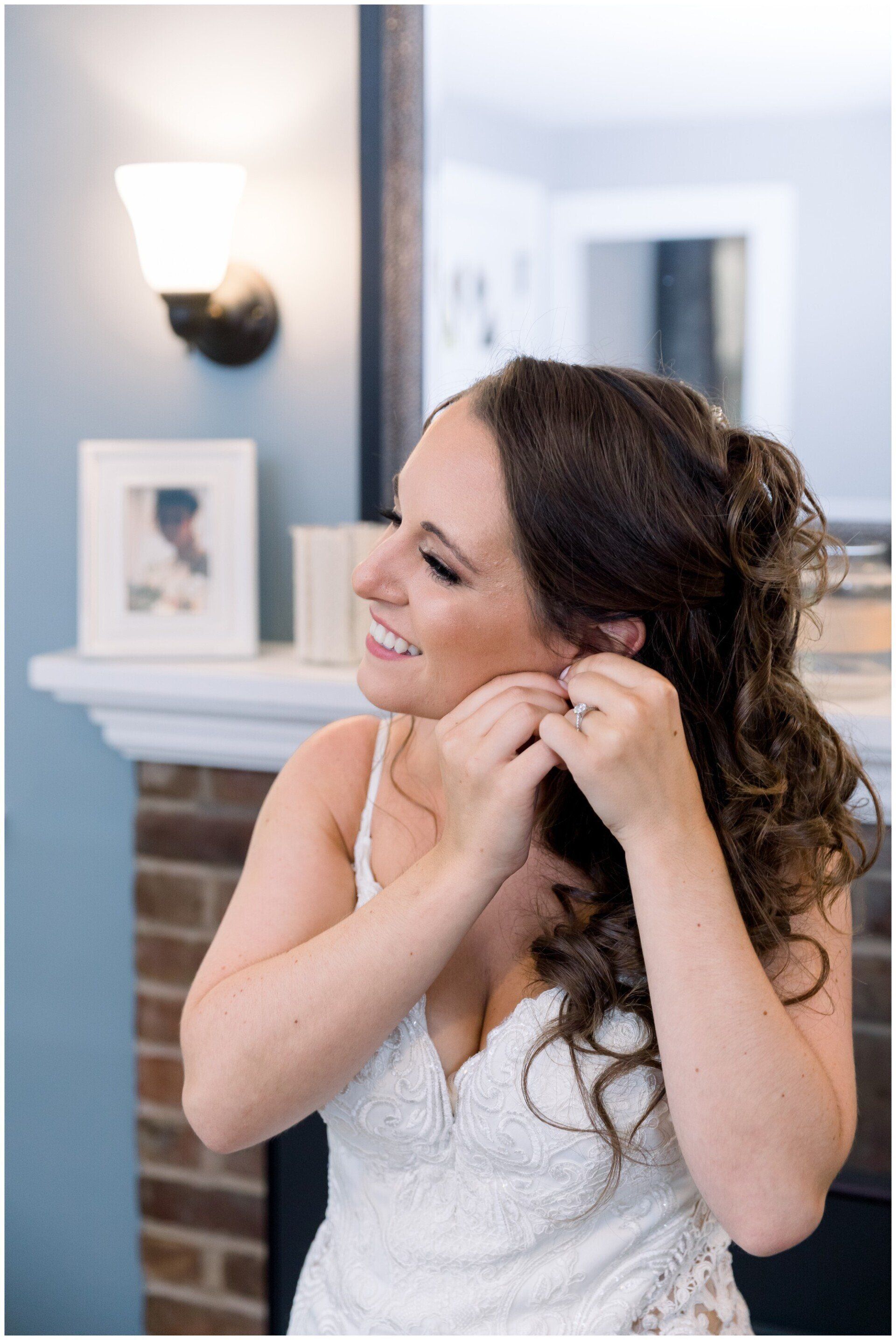 Woman in a white dress fastening an earring in a mirror-lit room