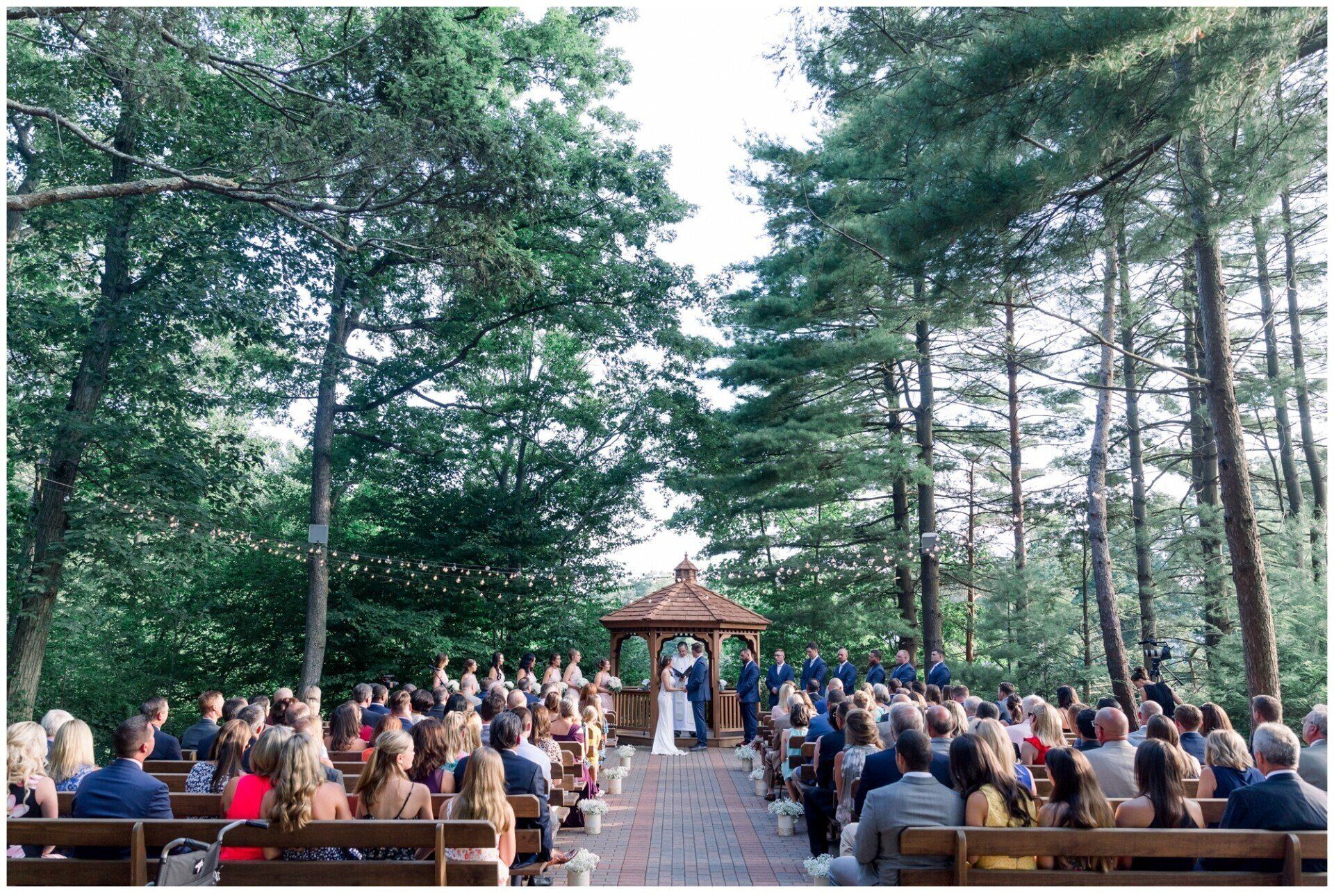 Outdoor wedding ceremony in a forest clearing with guests seated under tall trees