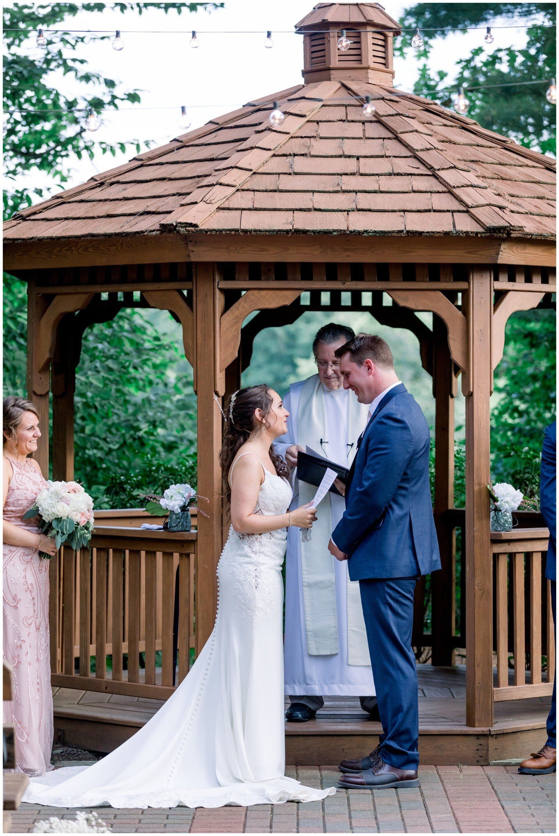 Bride and groom exchanging vows in a wooden gazebo at an outdoor wedding ceremony