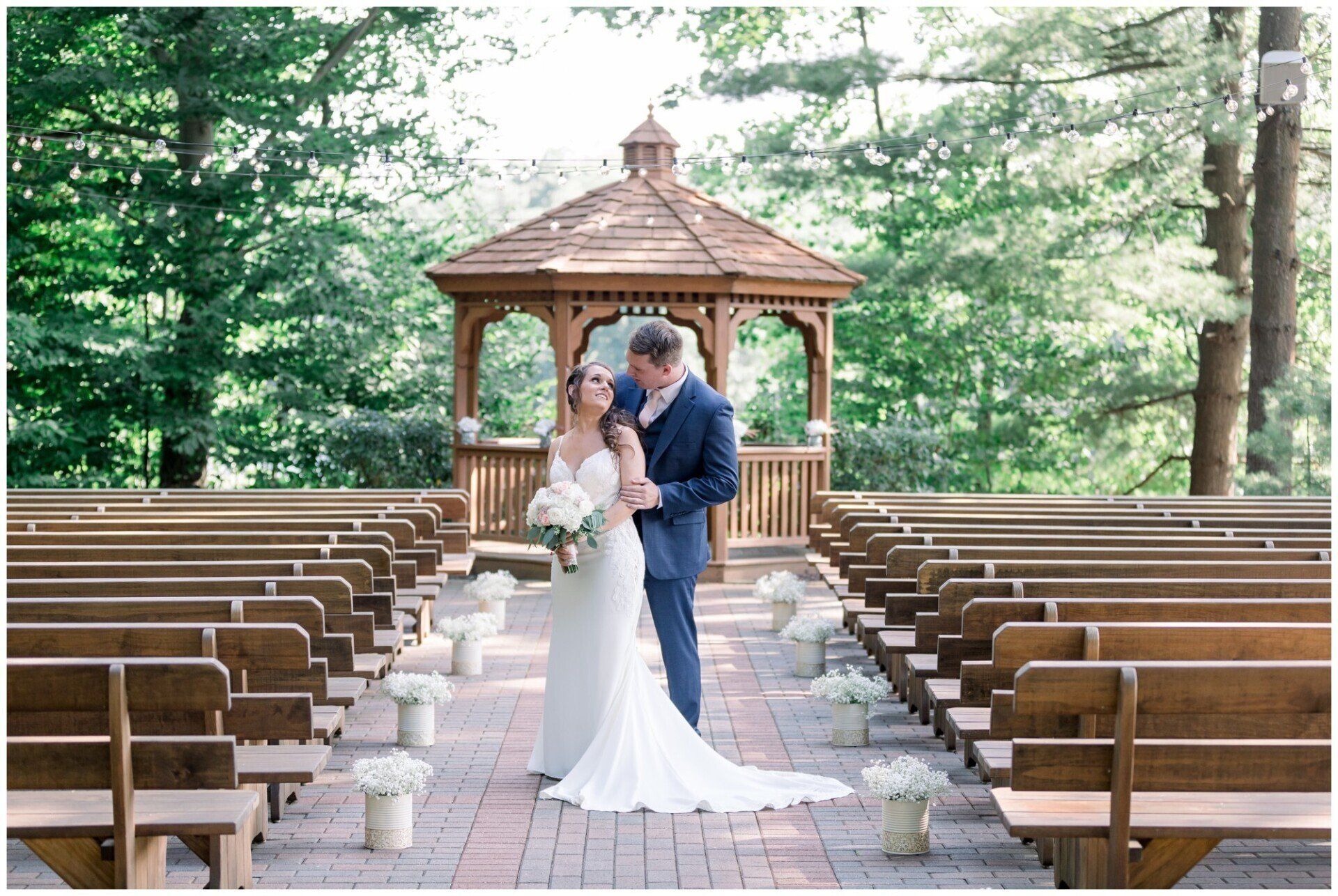 Bride and groom kissing in a gazebo among rows of benches in a forest chapel