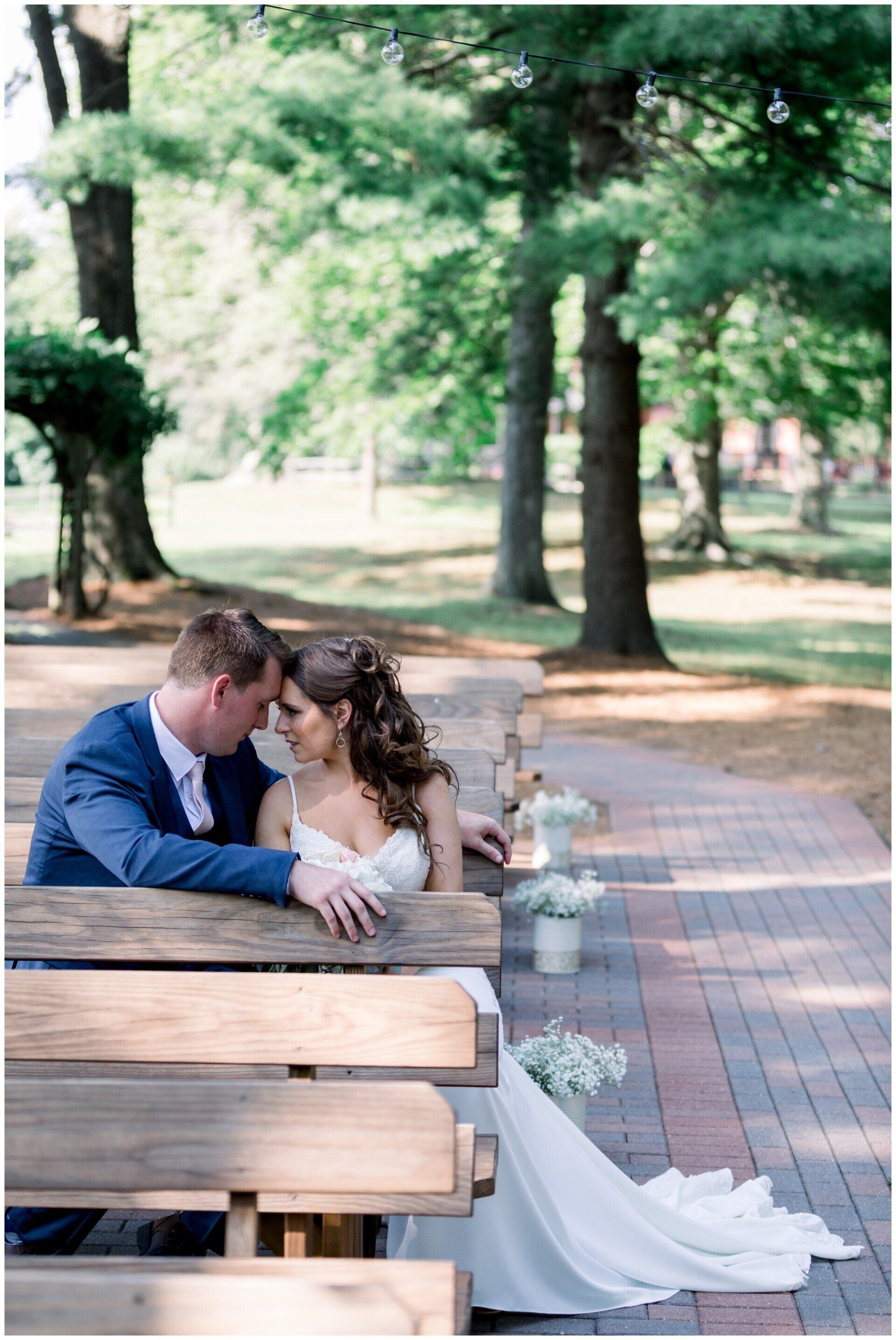 Couple seated on a park bench, holding each other in a tree-lined outdoor setting.