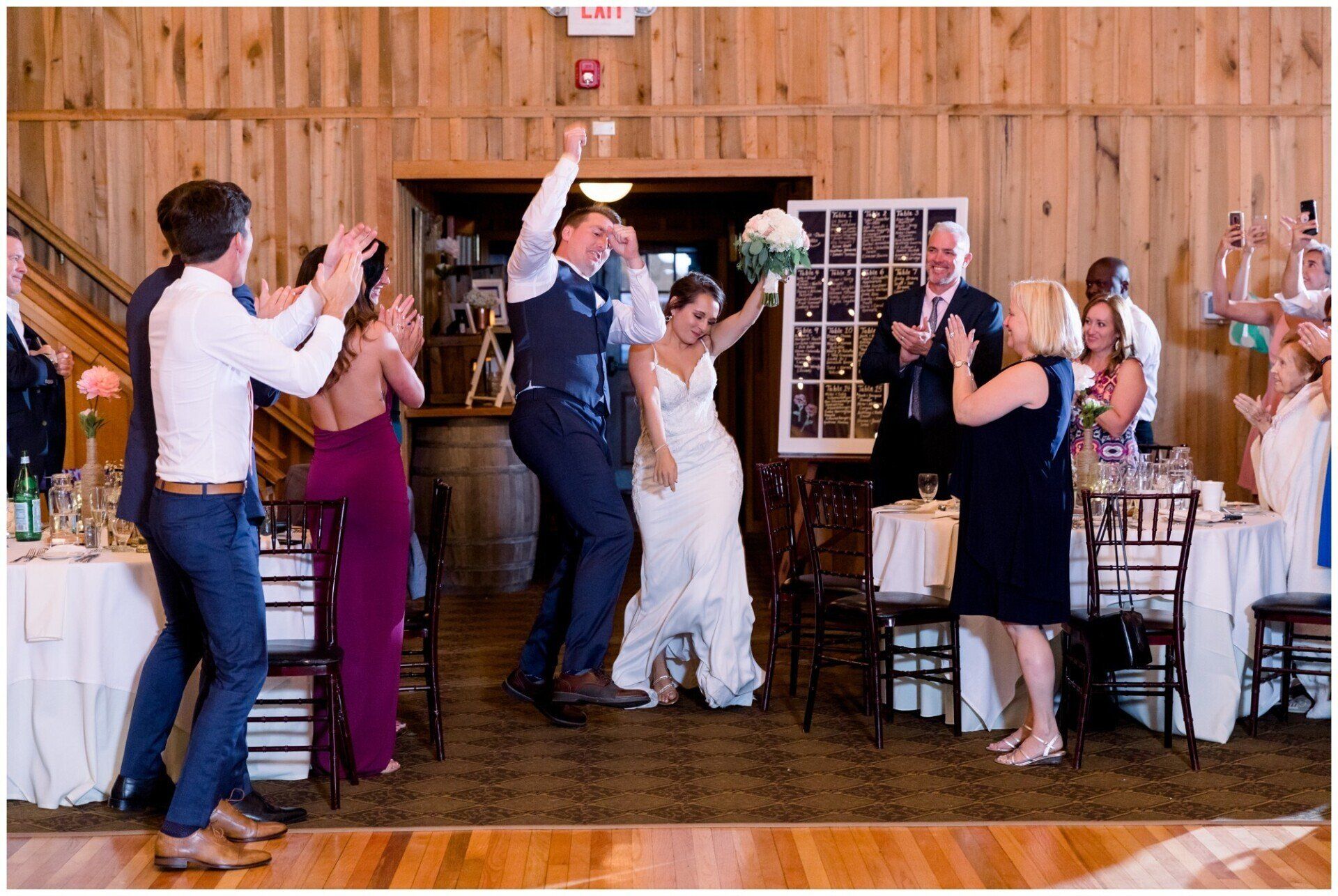 Wedding guests cheering and raising glasses as the bride and groom celebrate on a rustic wooden dance floor