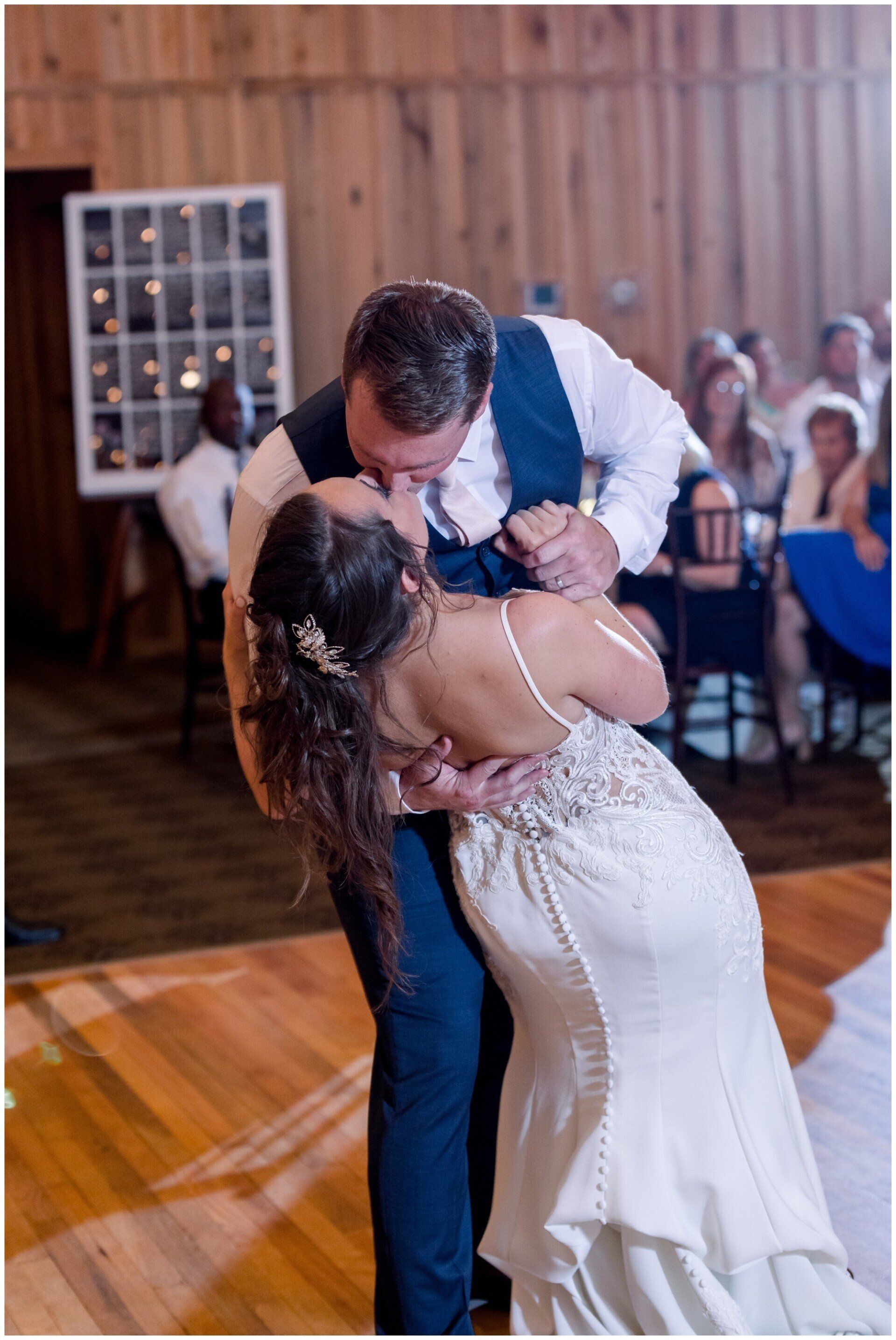 A couple dances closely at a wedding reception, with the bride in a white gown dipping back as the groom leans in.