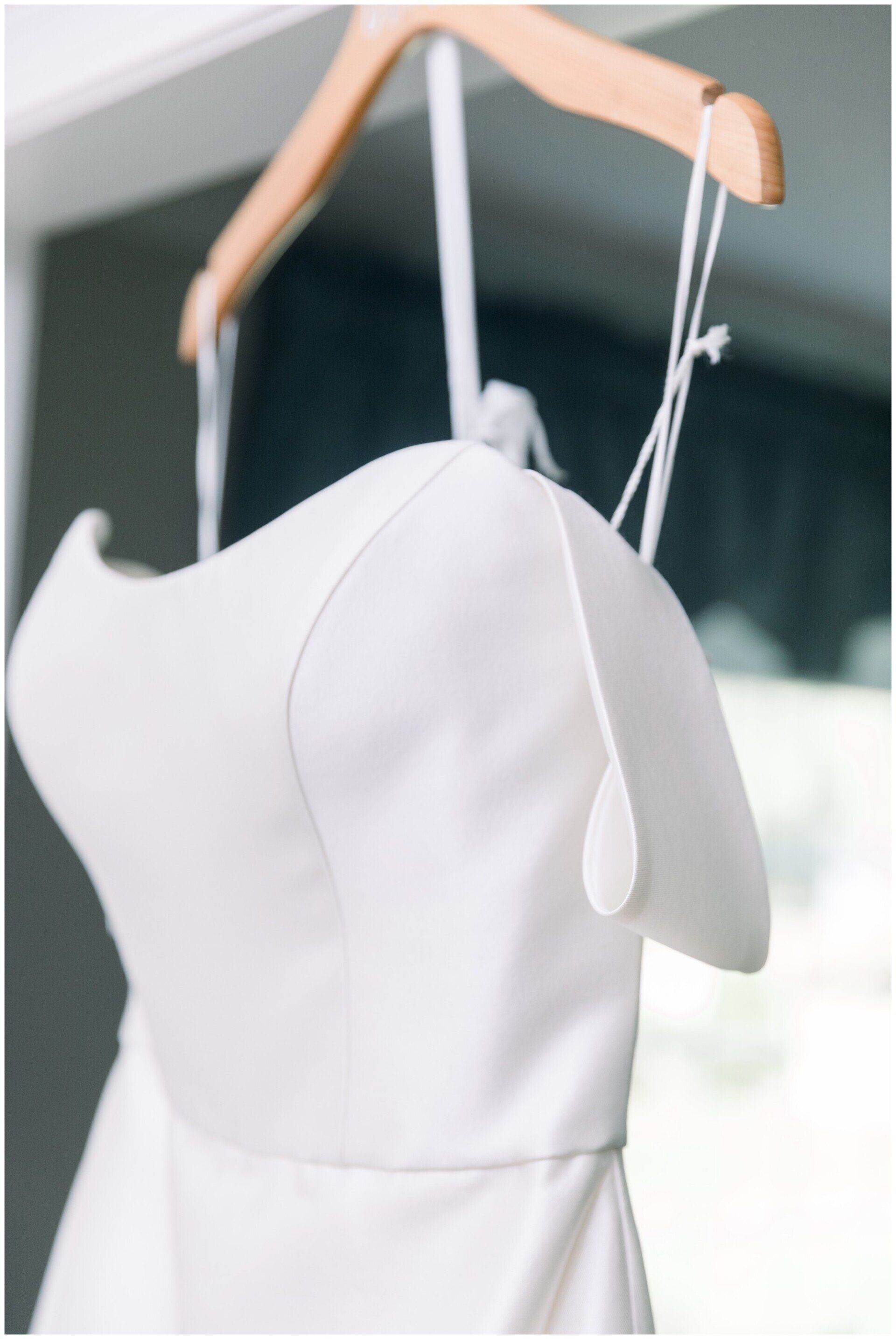 White dress on a wooden hanger against a softly blurred indoor background.