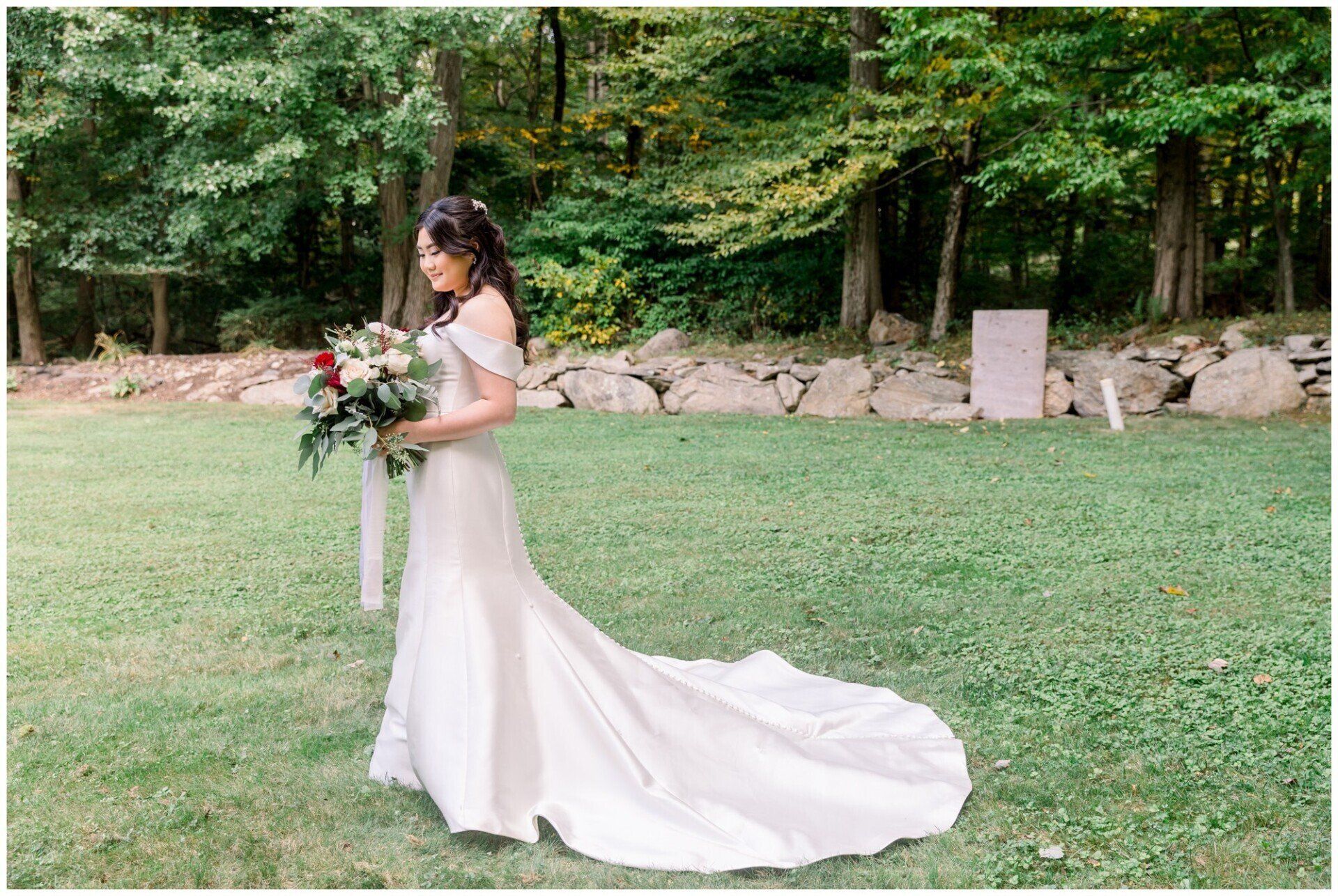 Bride in a white gown holding a bouquet in a grassy garden setting, with a long flowing train