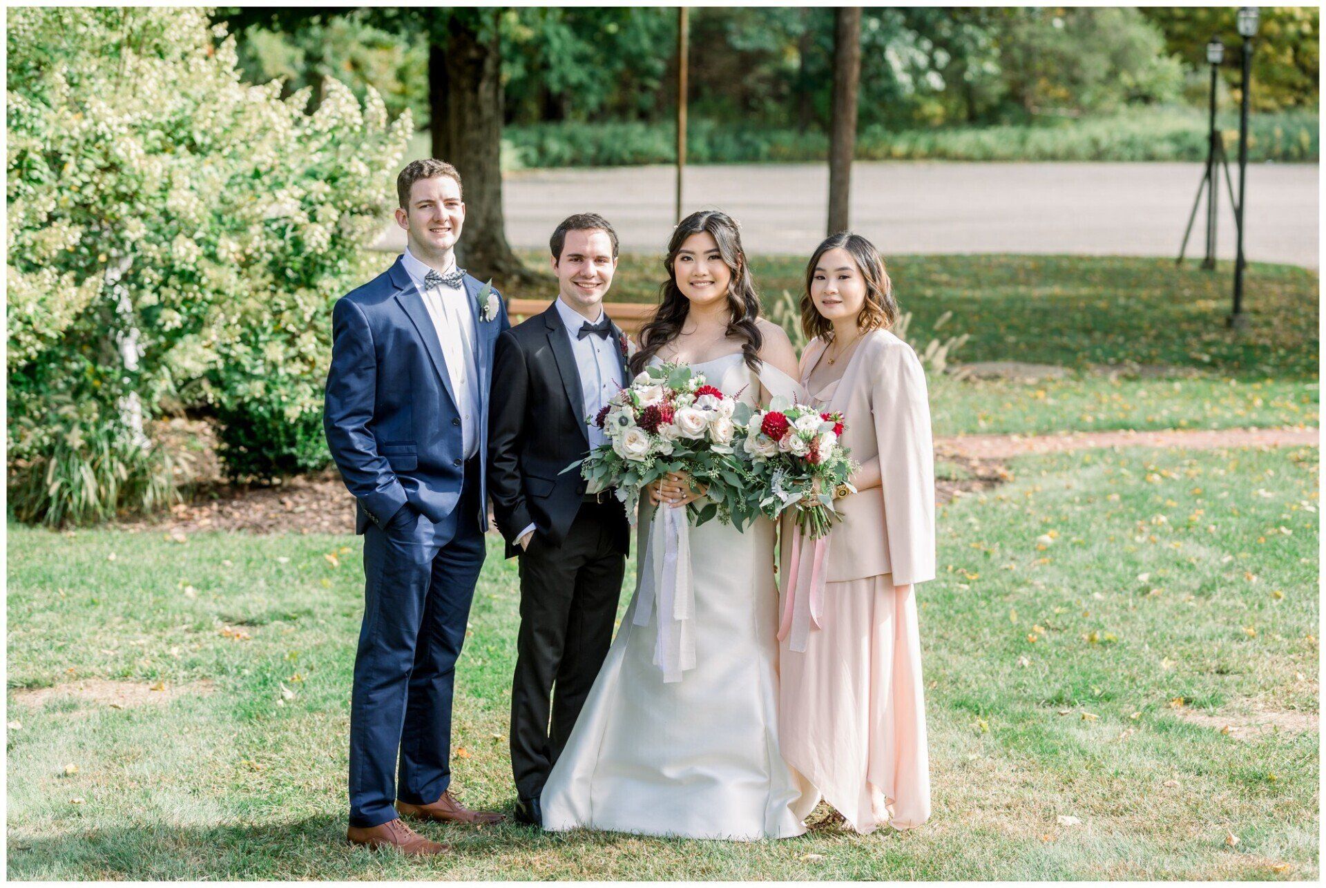 Four people stand outdoors on grass, with the bride holding a bouquet and wearing a white dress.