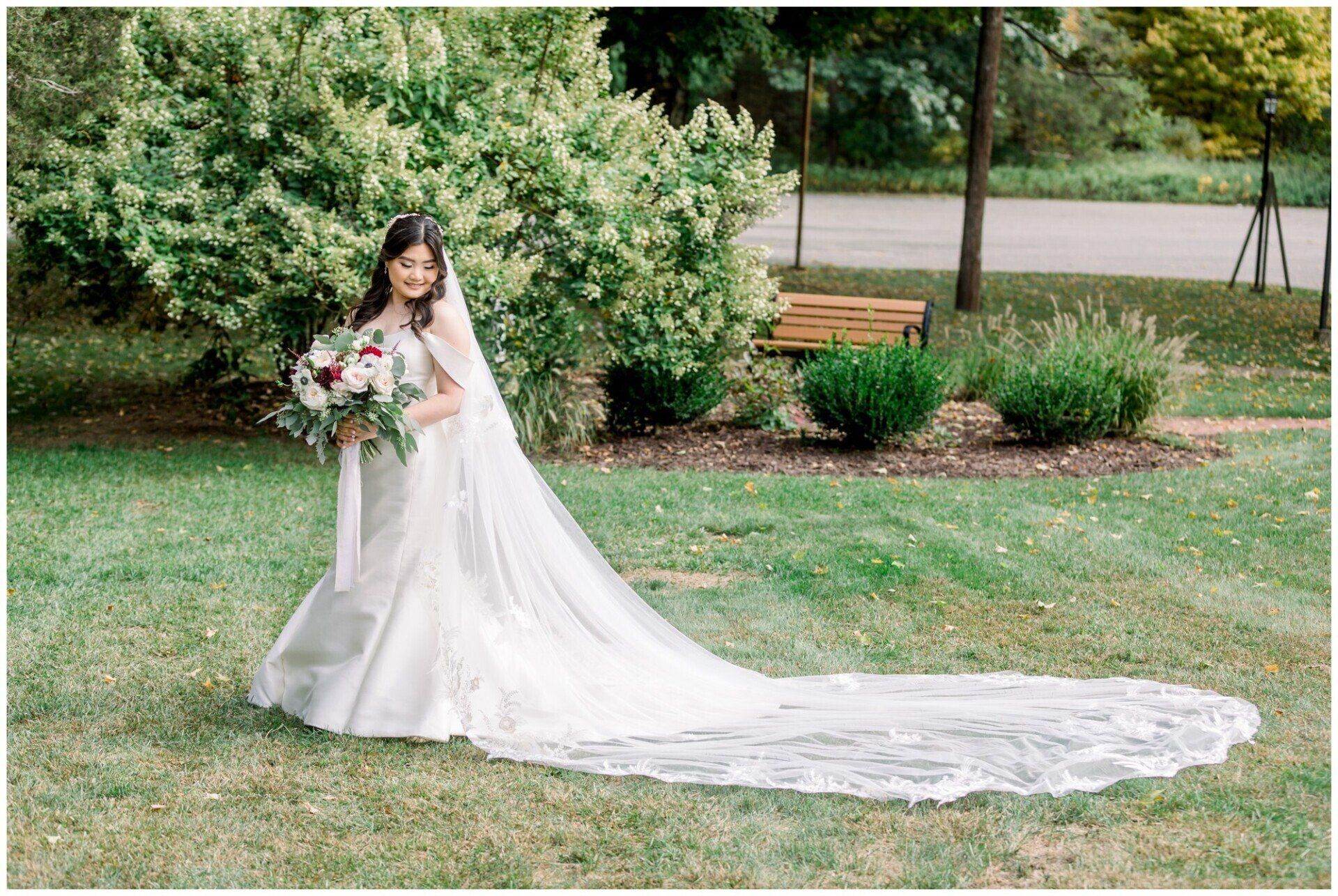 Bride in white gown holding bouquet in a garden, with a long train spread across the grass.