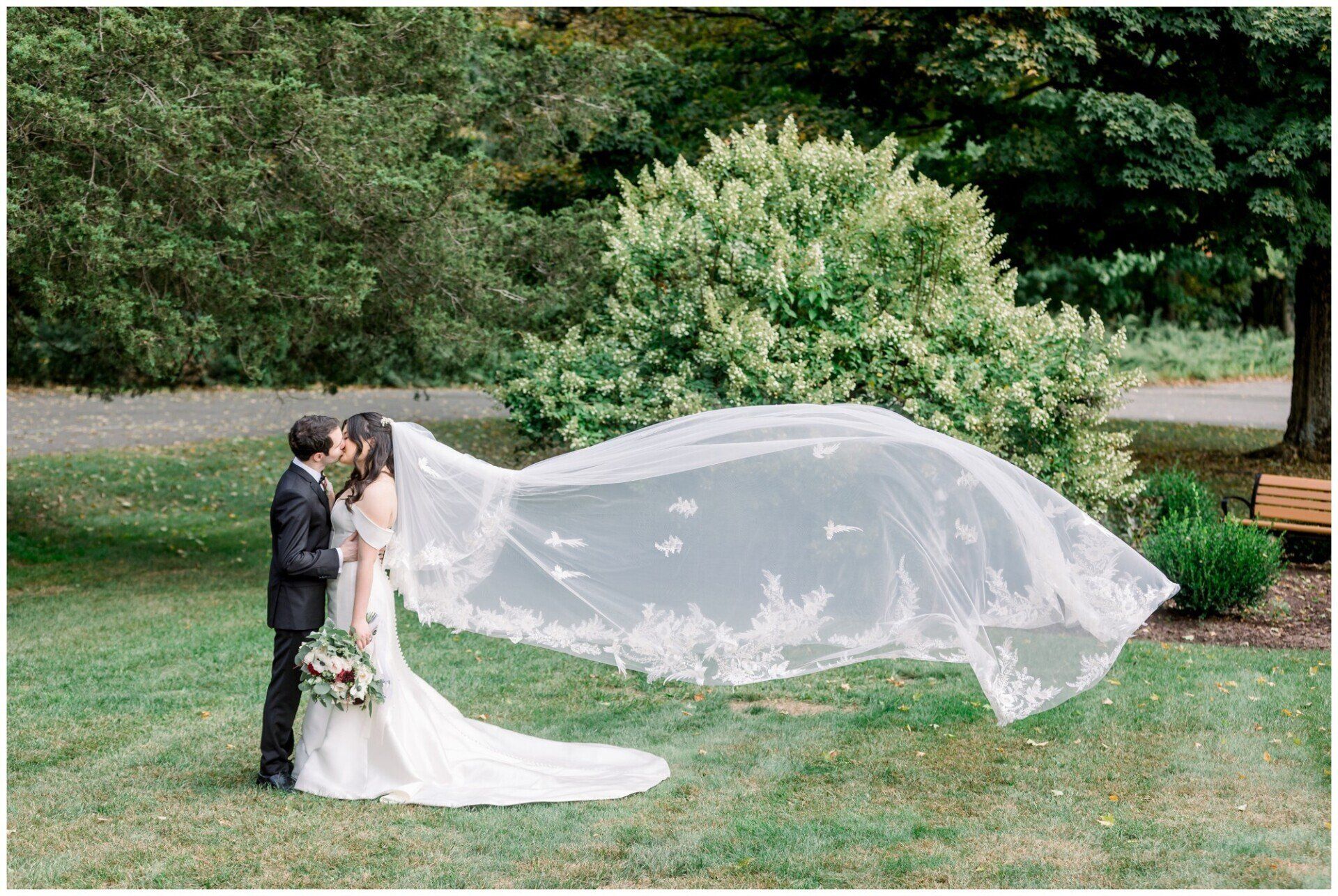 Bride and groom kissing in a garden, with the bride’s veil blowing in the wind