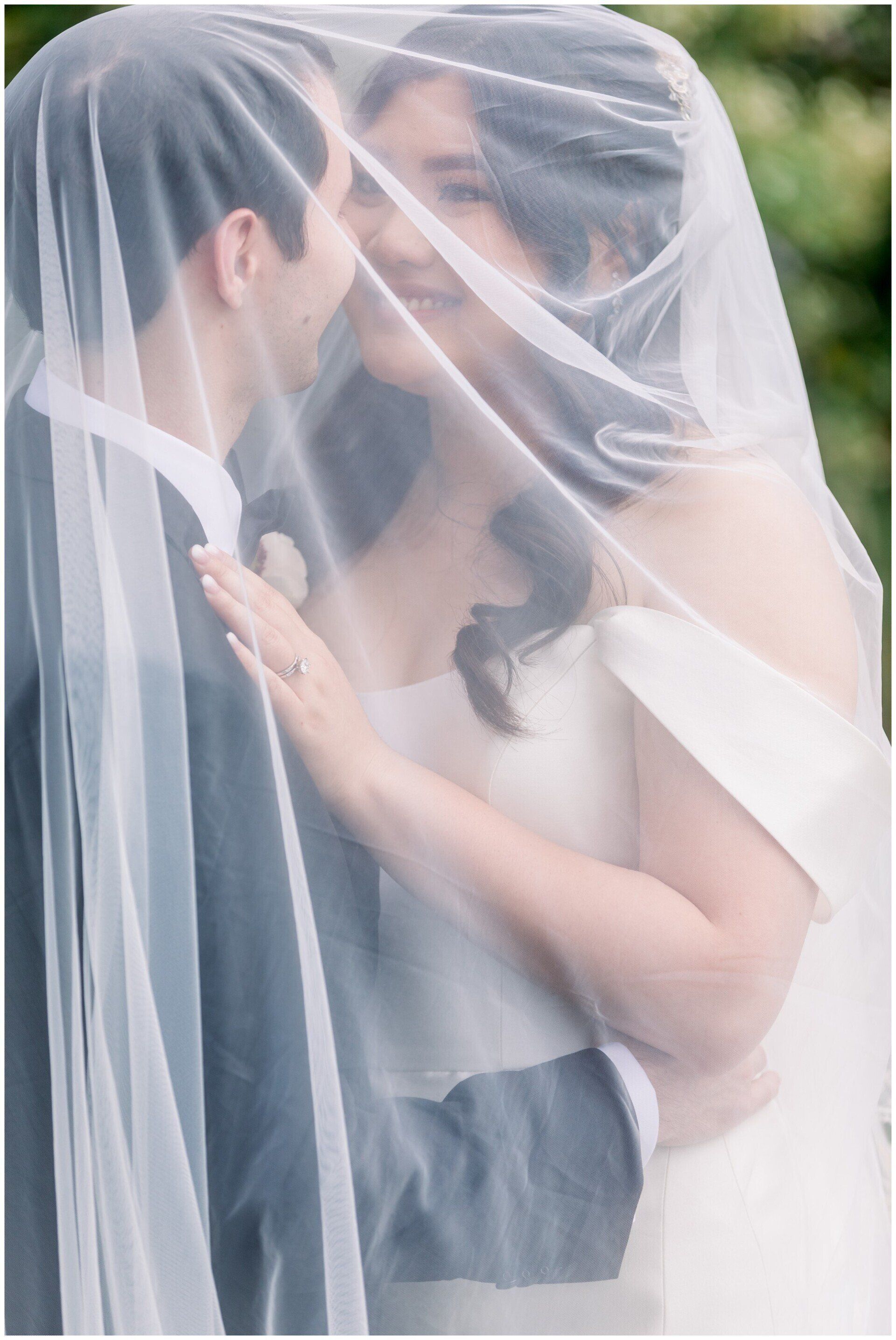 Bride and groom sharing a kiss under a white veil outdoors