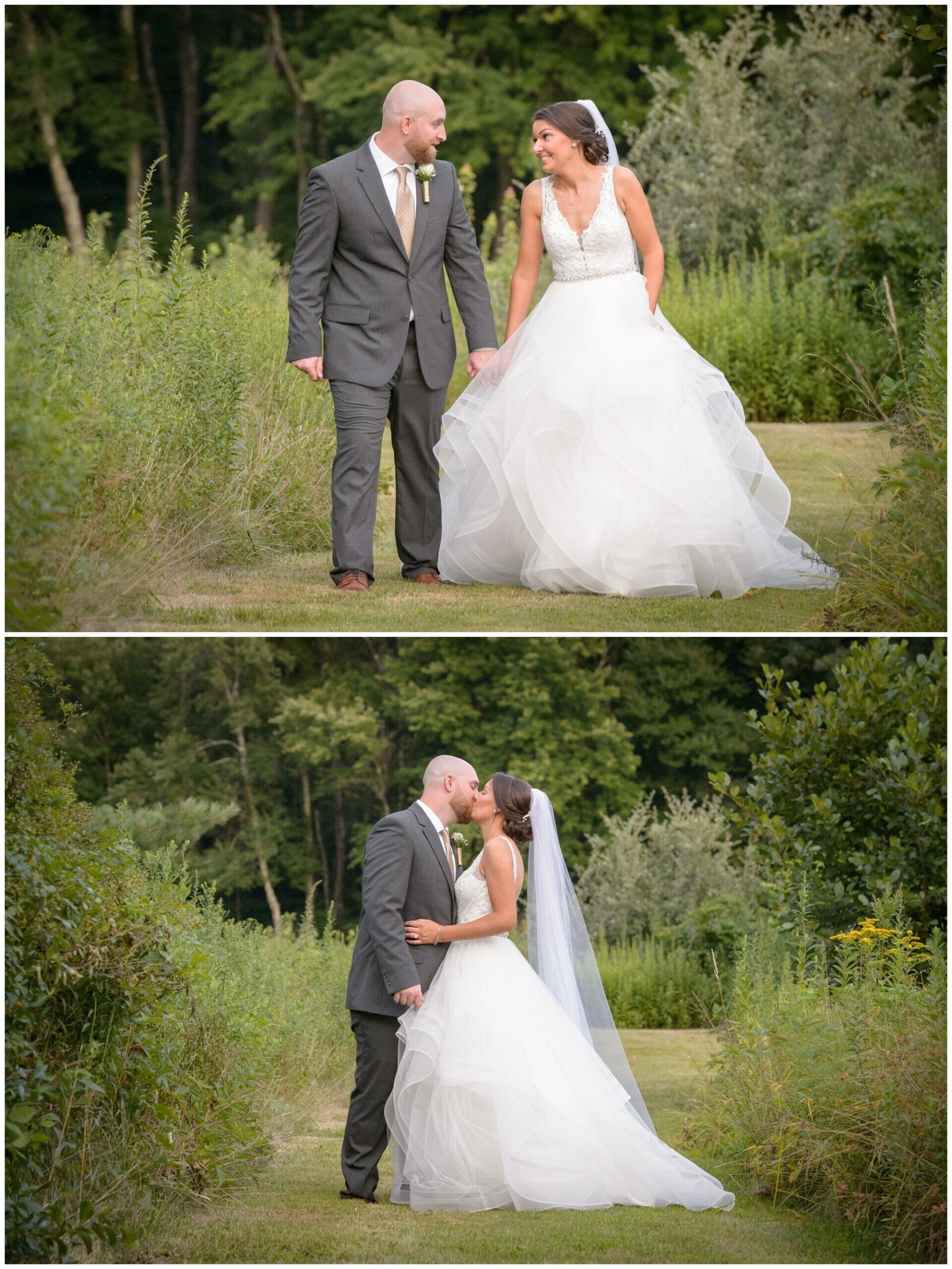 Bride and groom in wedding attire standing and kissing on a grassy path surrounded by trees