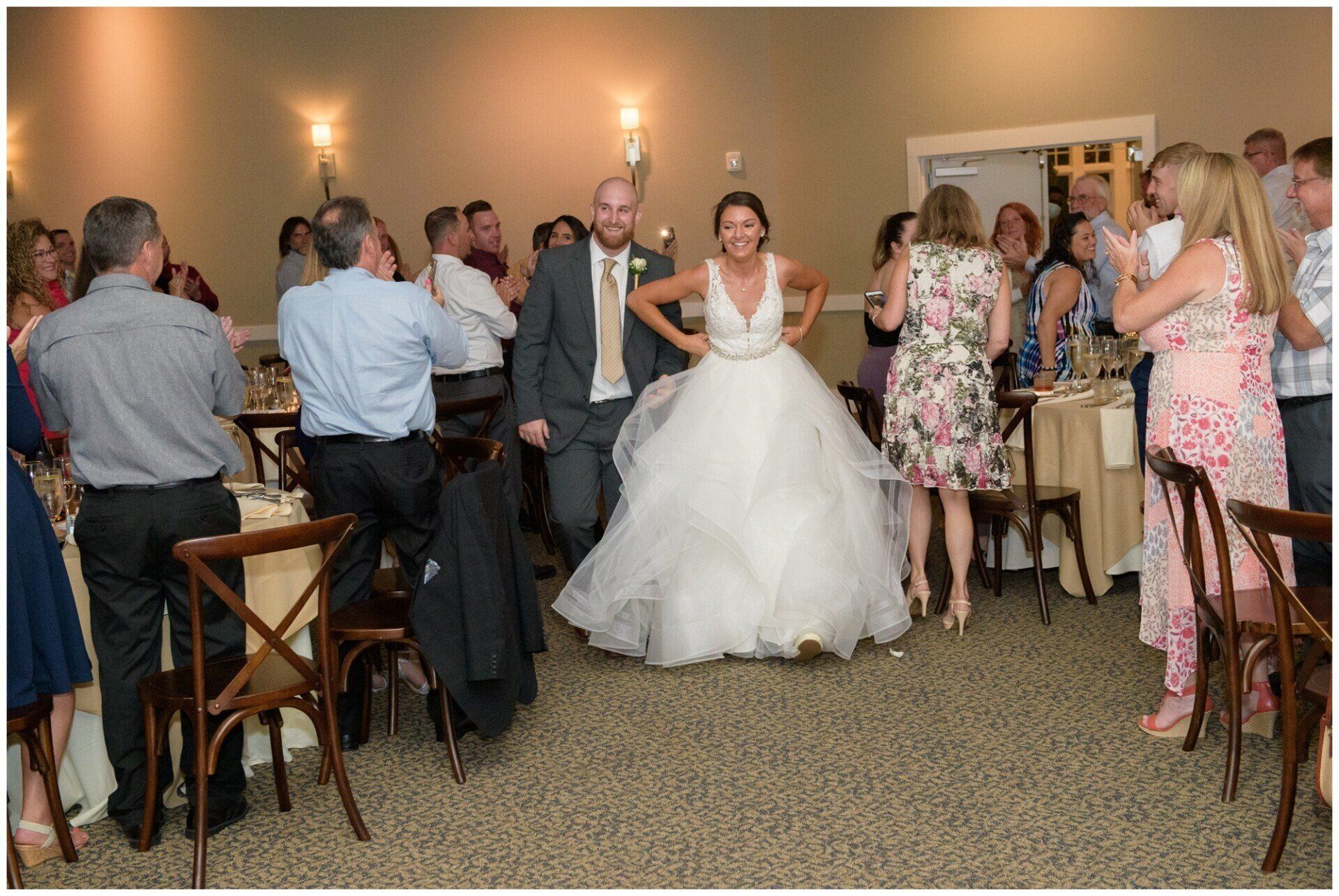 Bride in a white gown and groom walk through a banquet hall lined with applauding guests