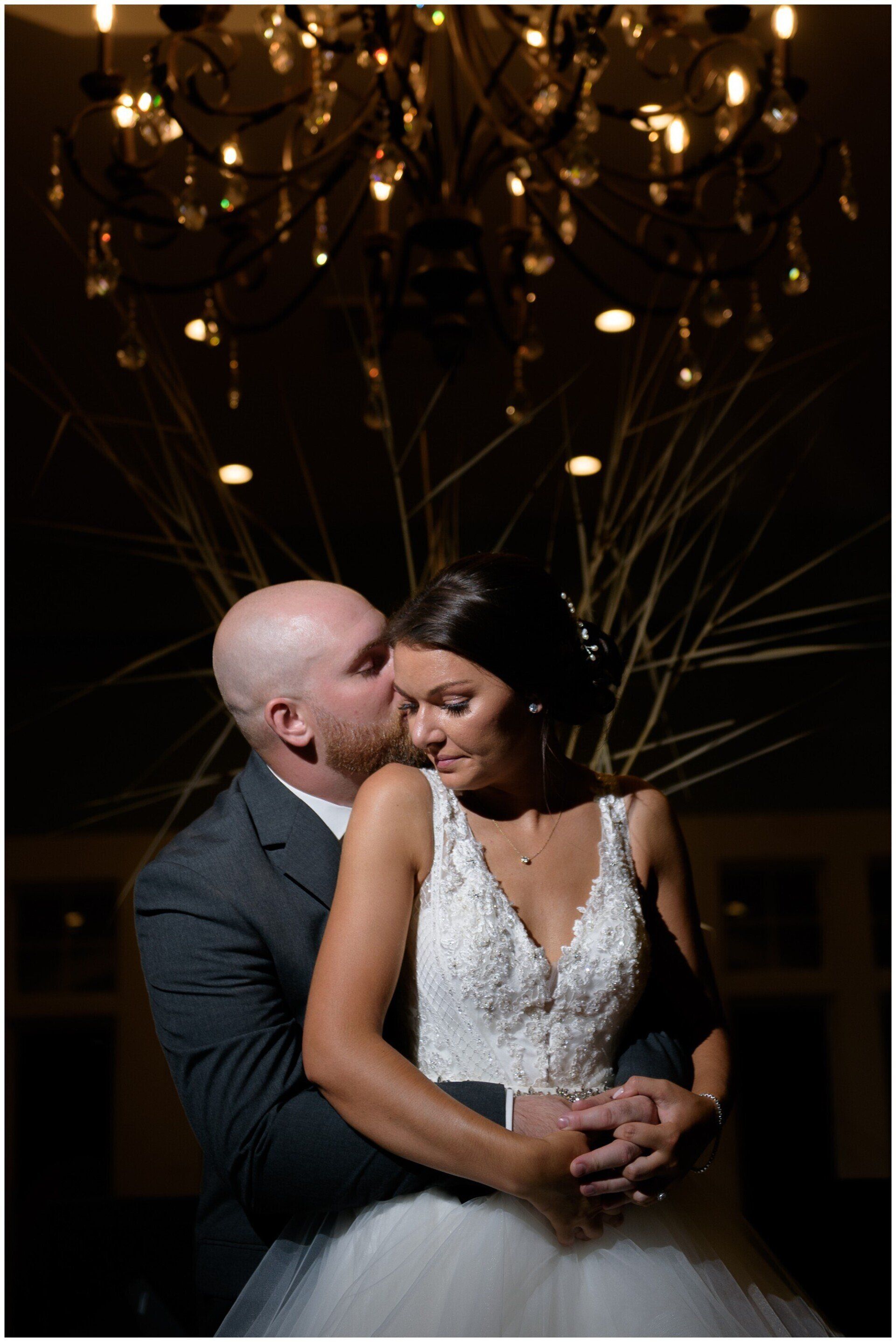 Couple embracing at a dimly lit wedding reception, with chandeliers glowing overhead