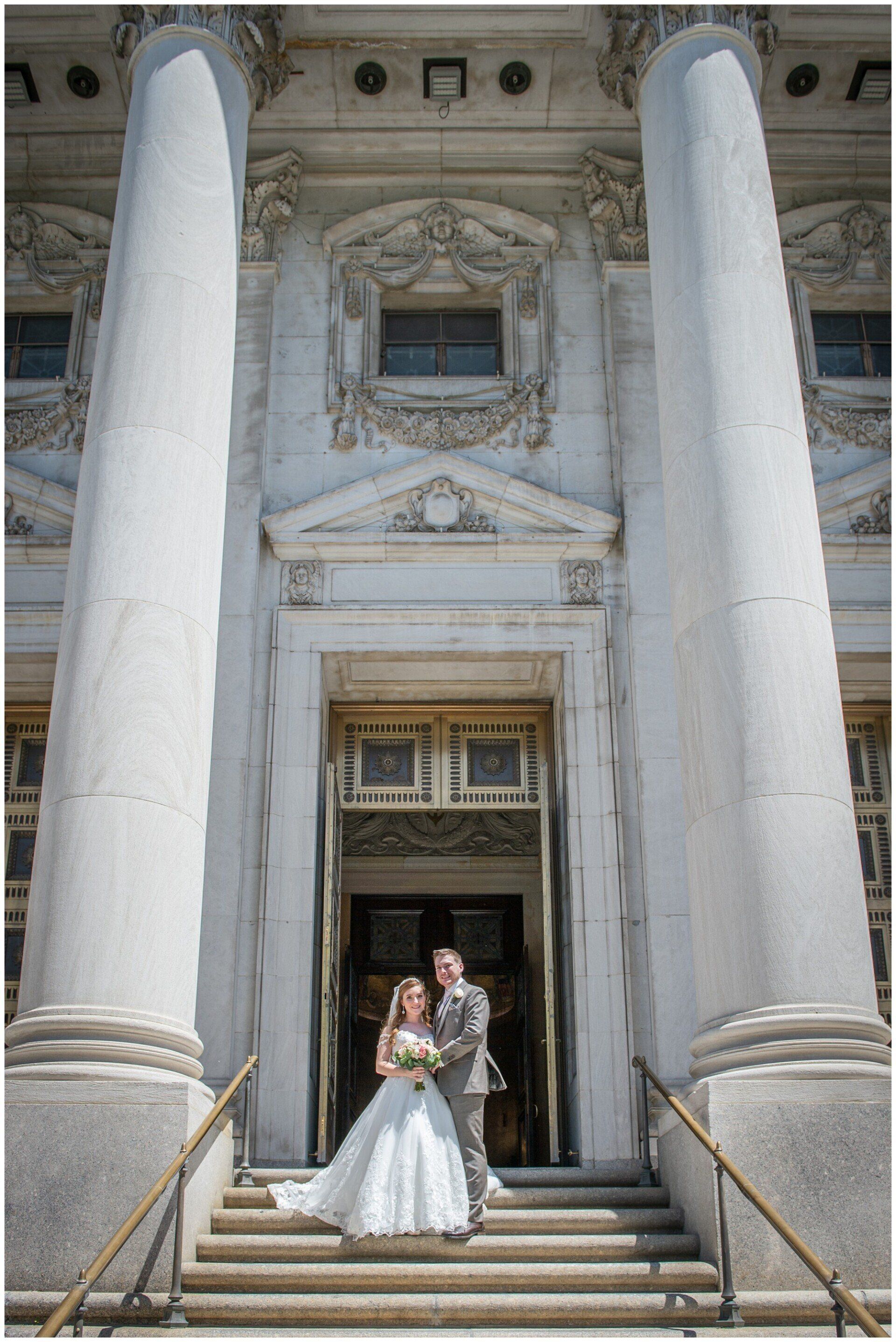 Bride and groom pose on steps of an ornate building with tall white columns