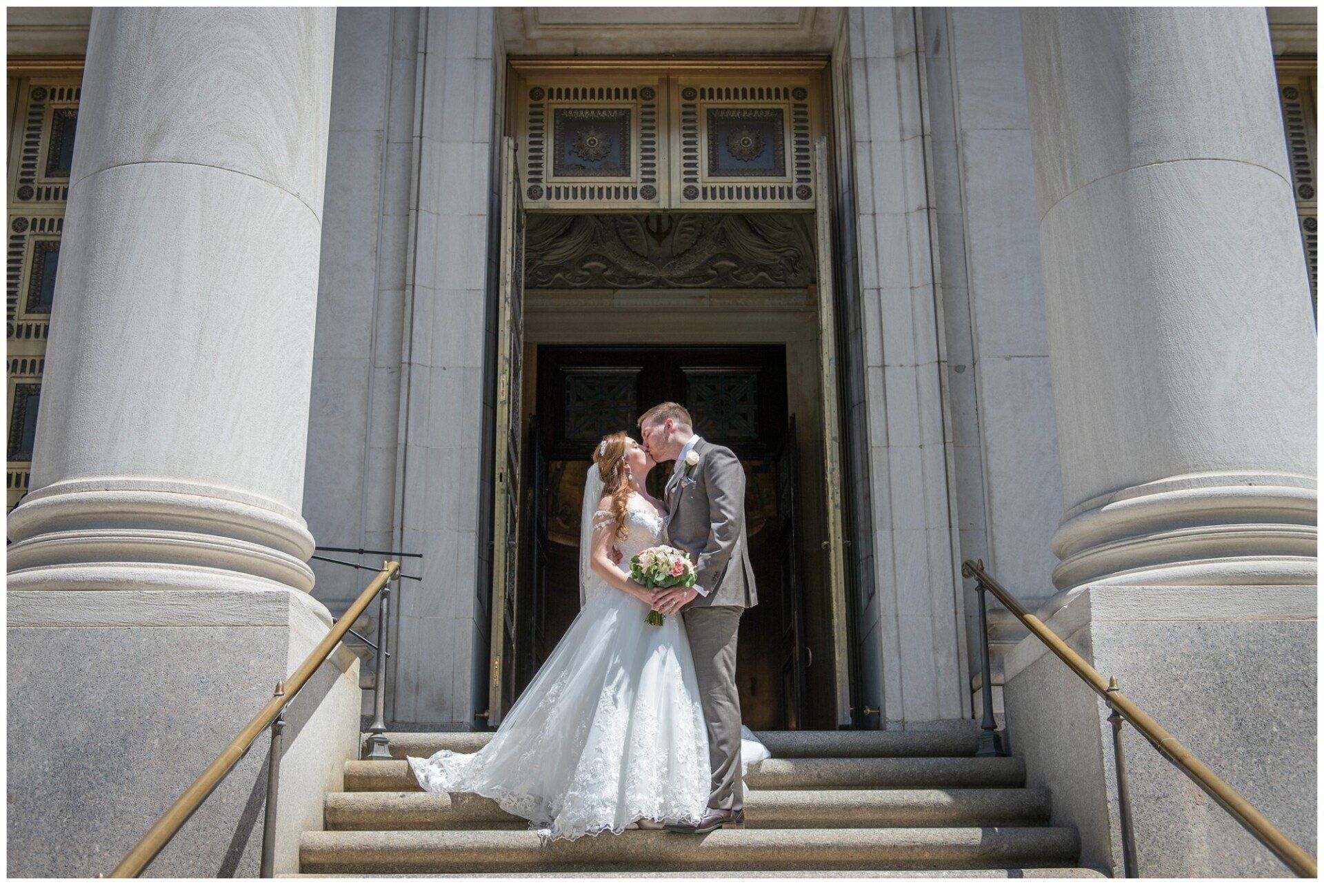Bride and groom standing on courthouse steps, embracing in wedding attire.
