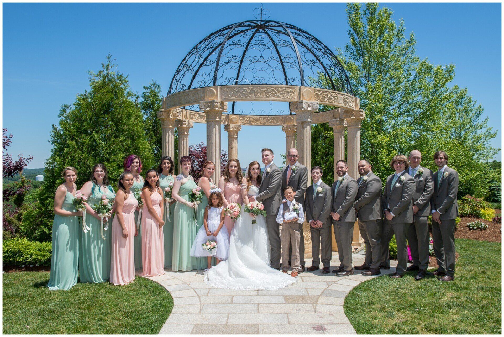 Wedding party posed in front of a gazebo, bride in white and bridesmaids in pastel dresses.