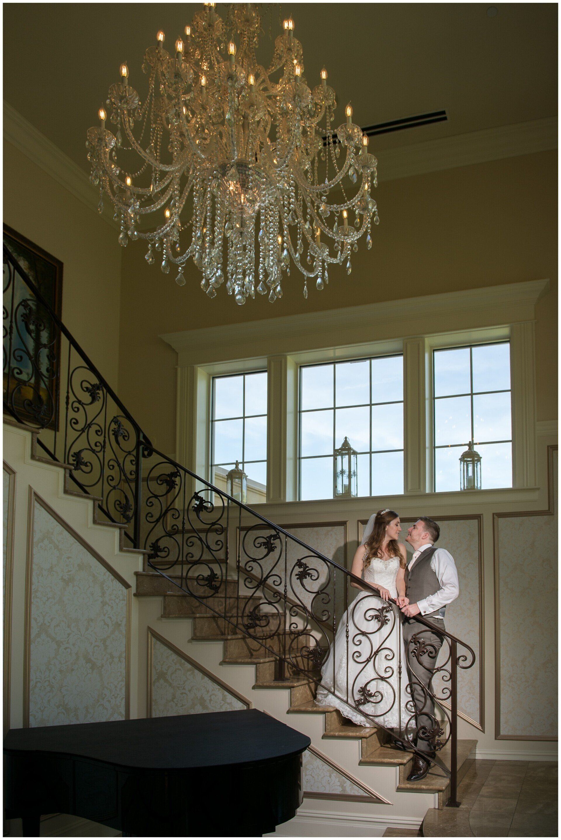 Couple embracing on a staircase beneath a crystal chandelier in a bright foyer