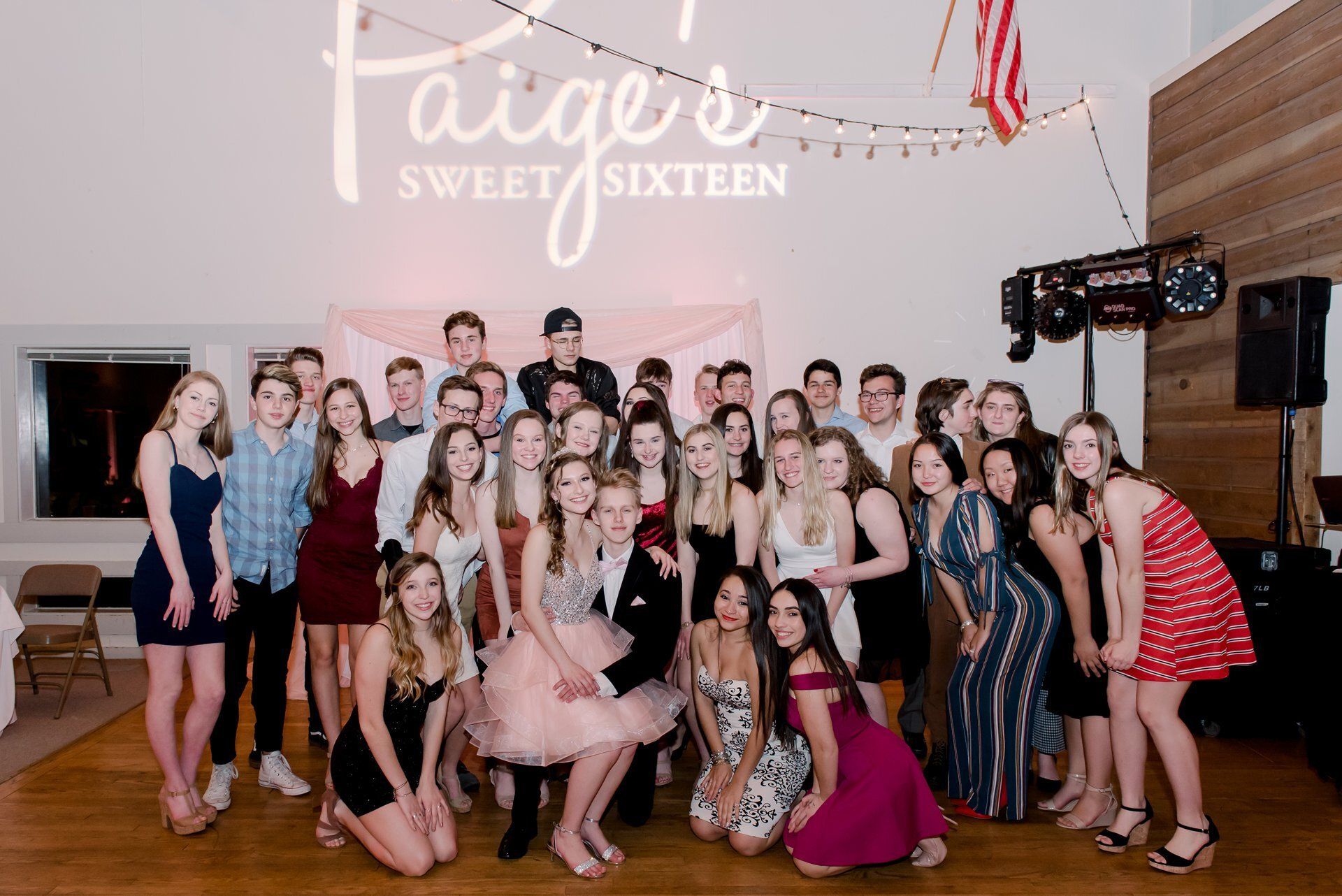 Group of teens posing on a dance floor beneath a “Sweet Sixteen” sign.