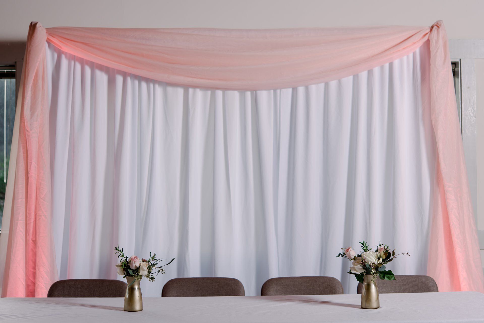 Pink draped backdrop with white curtains behind a decorated table with floral arrangements