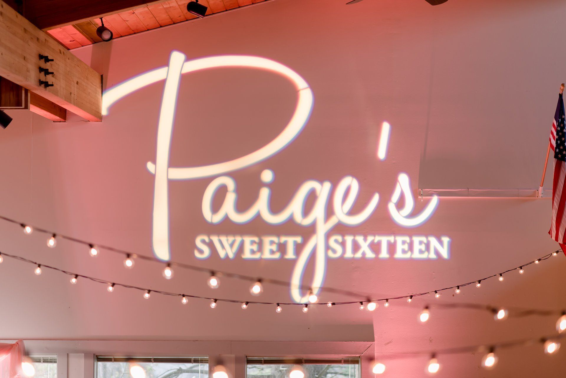 Pink party backdrop with string lights and glowing “Paige’s Sweet Sixteen” sign