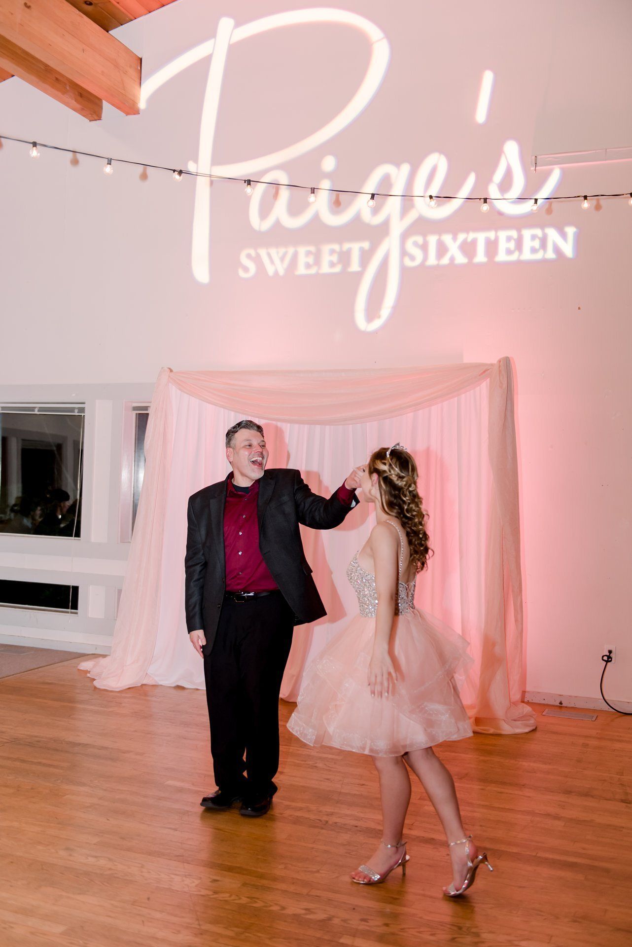 Girl and adult man dancing at a pink Sweet Sixteen celebration backdrop