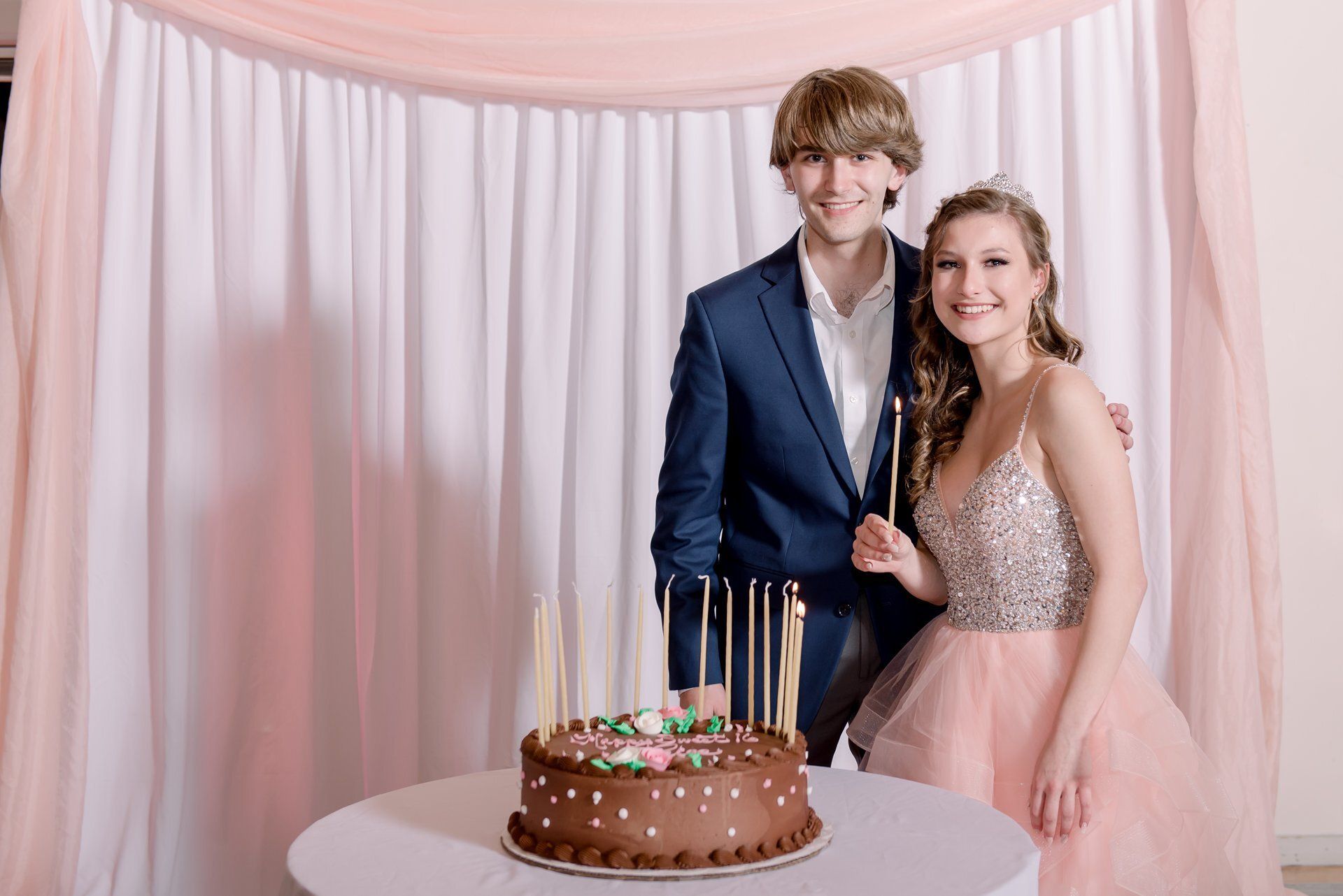 Couple posing behind a birthday cake in front of pink drapes