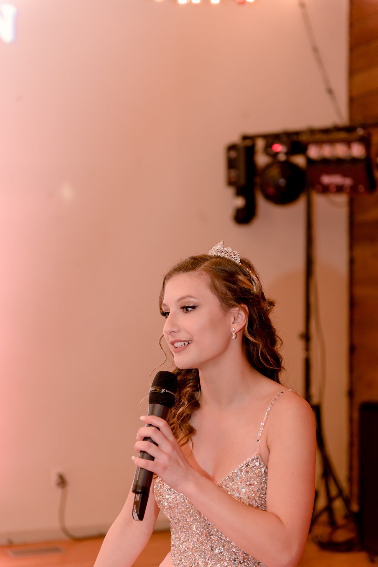 Young woman in a sparkly dress singing into a microphone on a softly lit stage