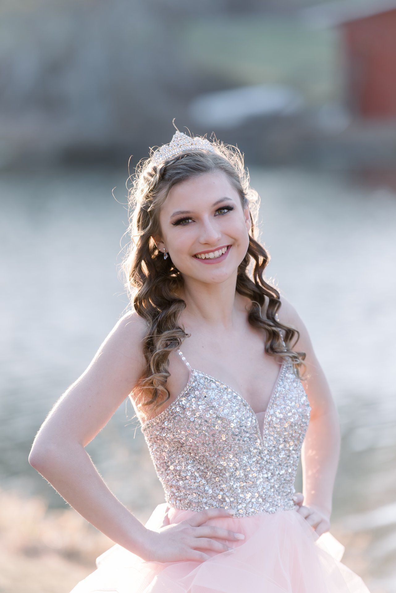 Smiling person in a sparkly pink dress posing outdoors with one hand on her hip
