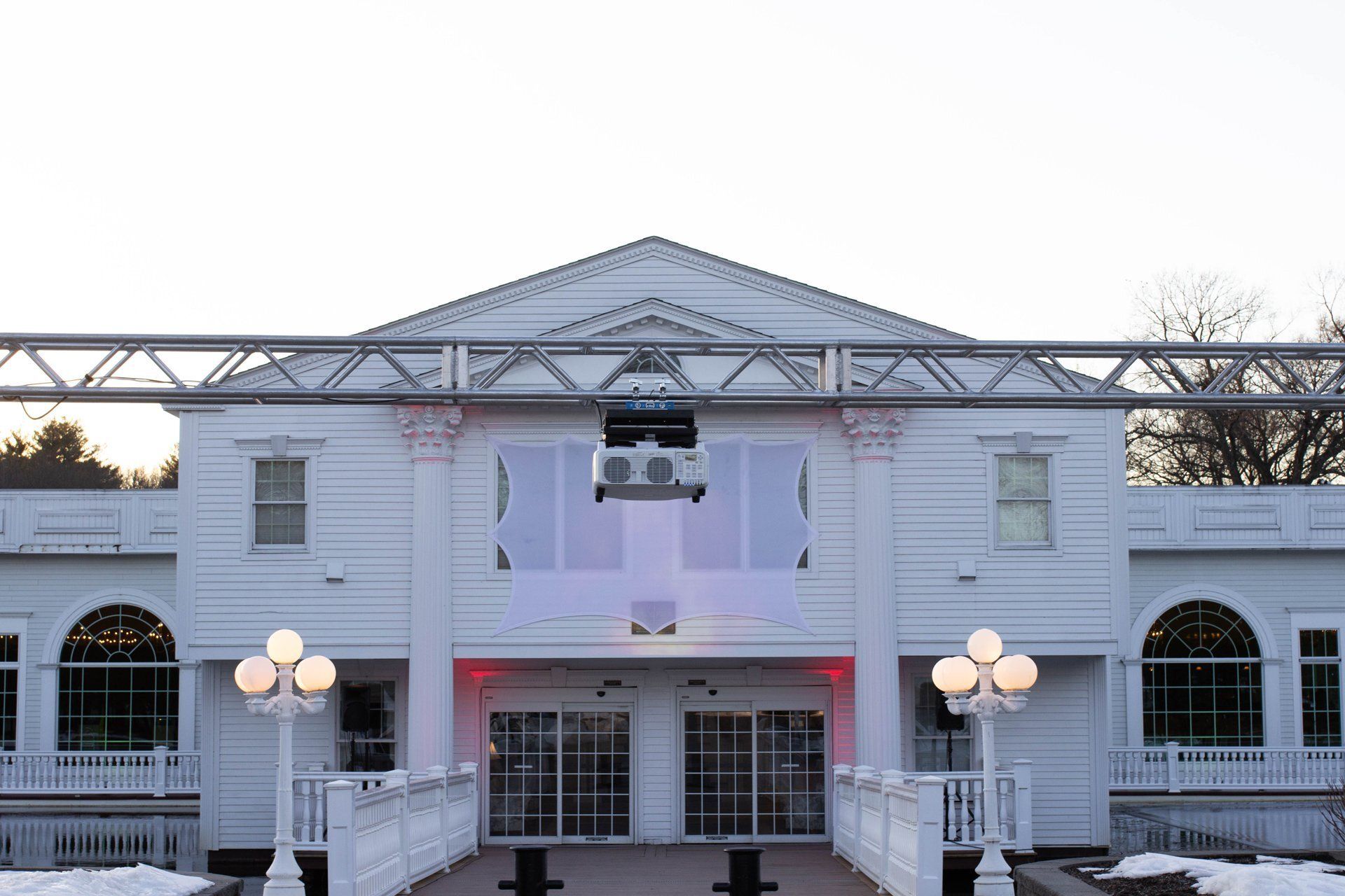 White building entrance with columns, arched windows, and lit globe lamps at dusk