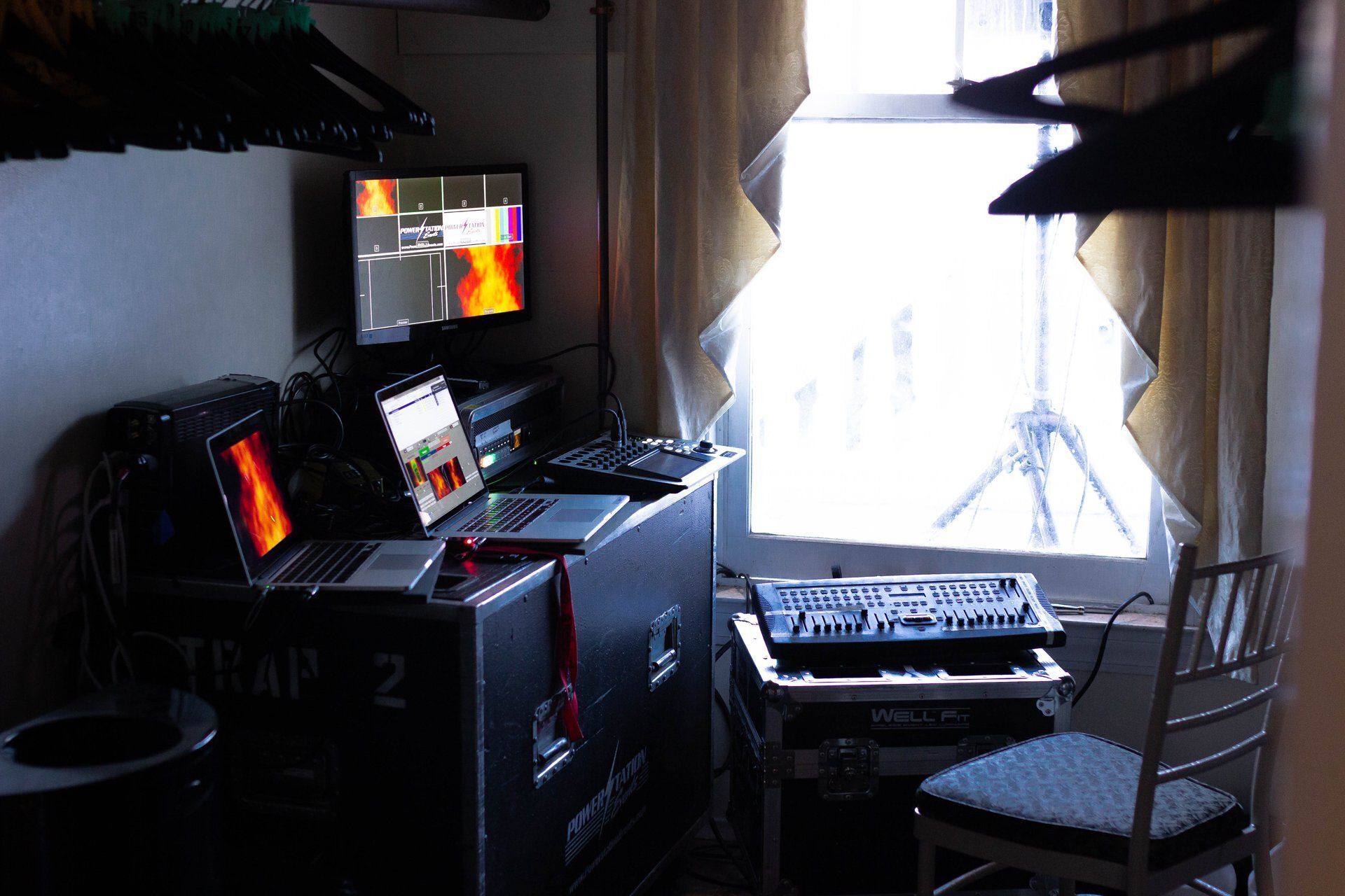 Small music production room with computer monitors, keyboard, chair, and bright window light