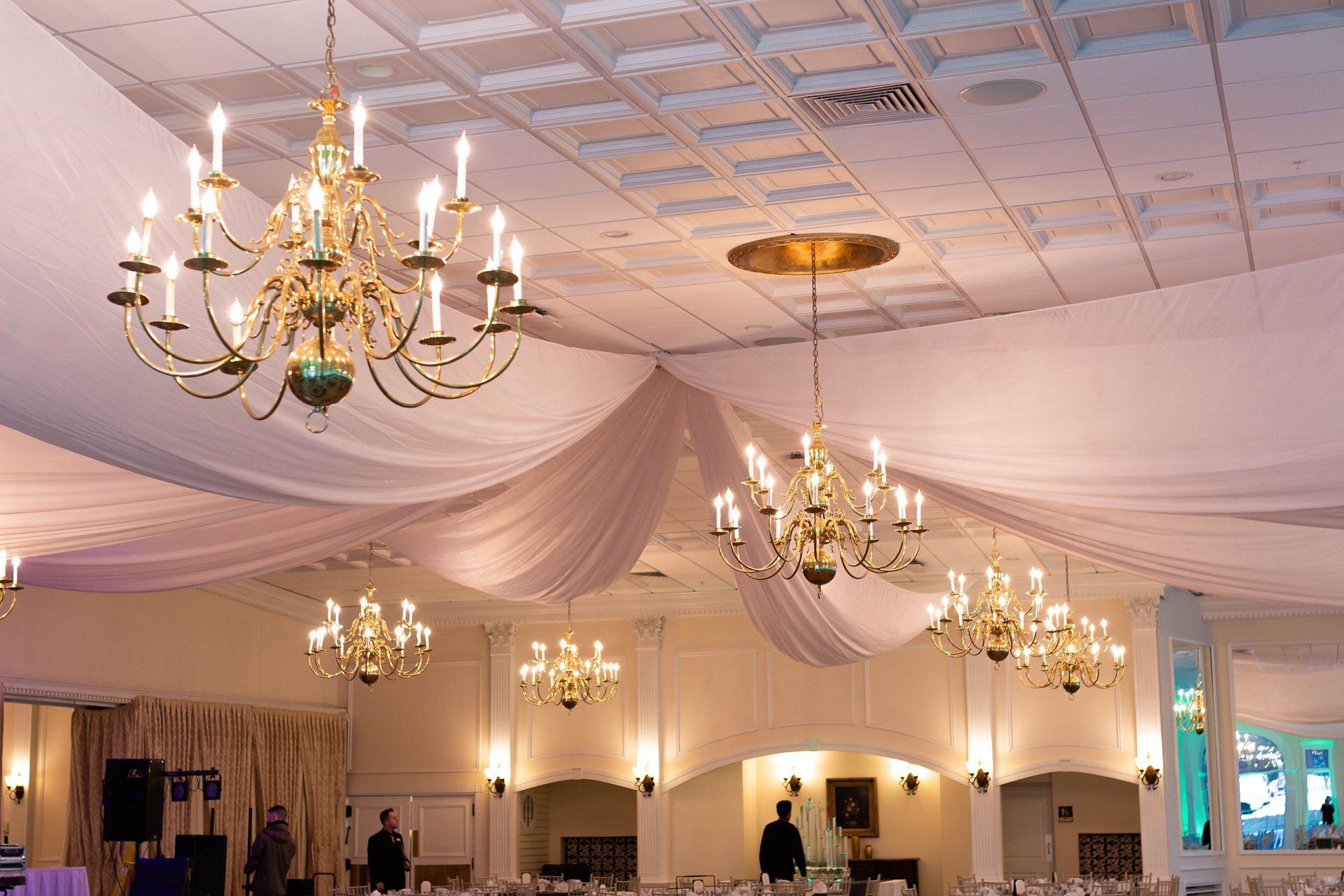Elegant banquet hall with white draped ceiling, gold chandeliers, and round tables set for an event