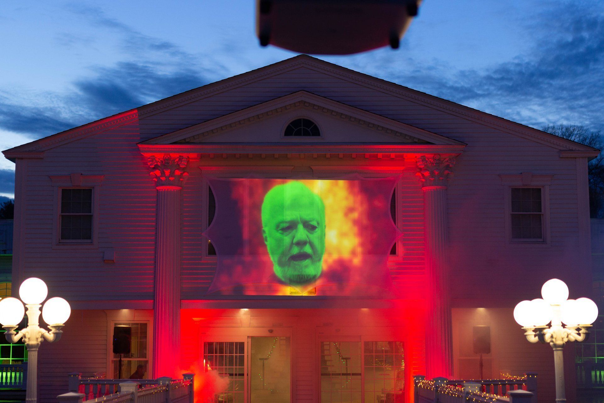 House facade lit red with a projected green face glowing on the front at night
