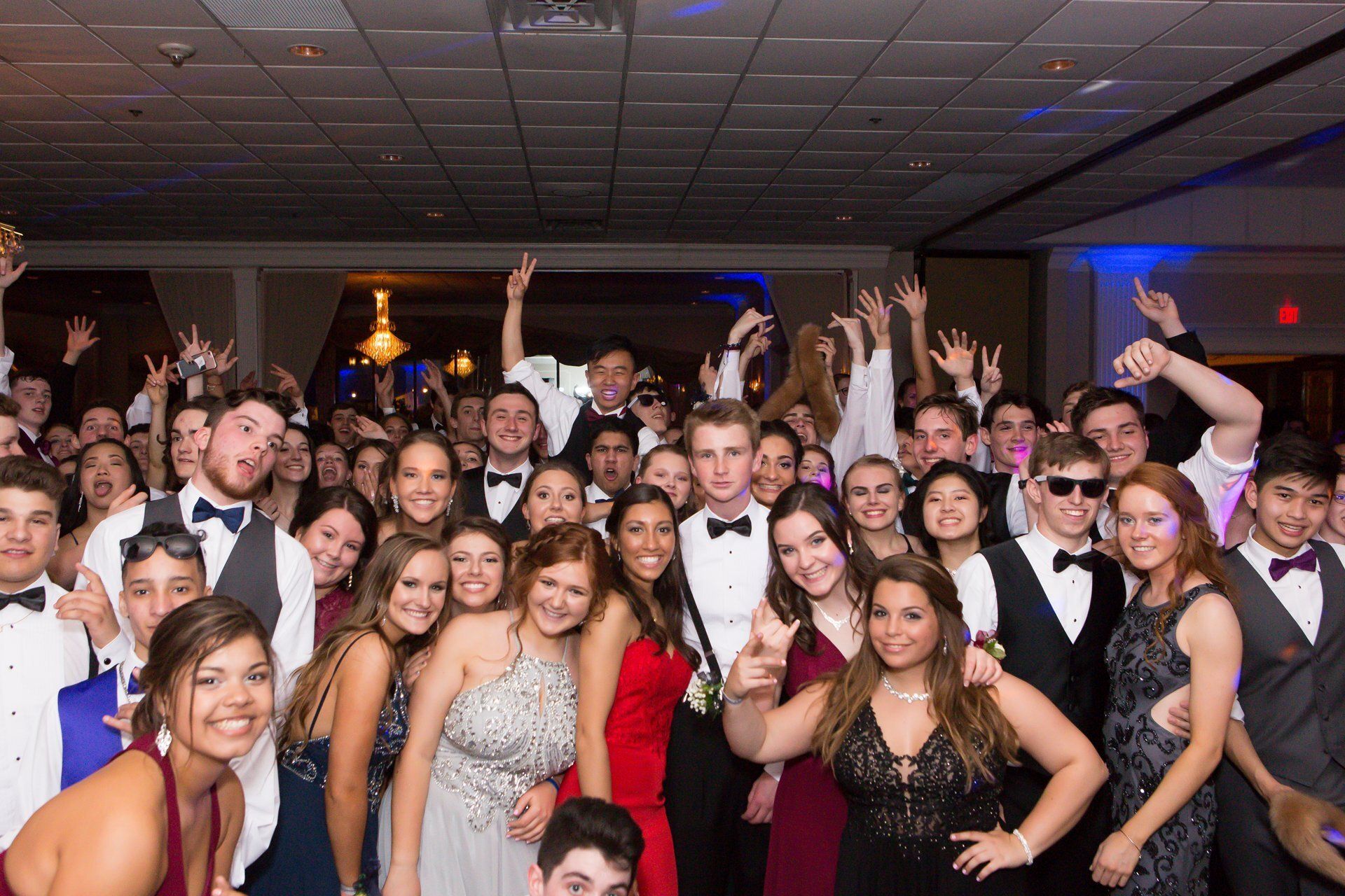 Crowd posing and dancing at a formal party, with hands raised under colorful club lights