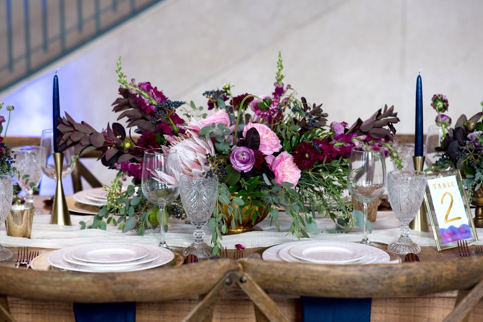 Decorated banquet table with pink and purple floral centerpiece, candles, glassware, and plates