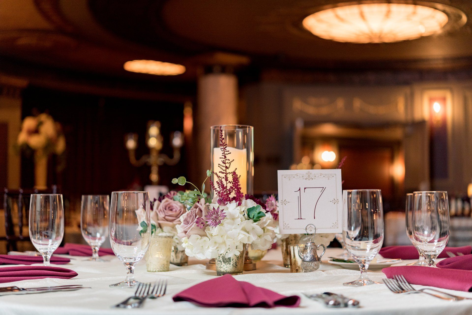 Elegant banquet table with pink napkins, floral centerpiece, candles, and table number 17 in a warmly lit hall
