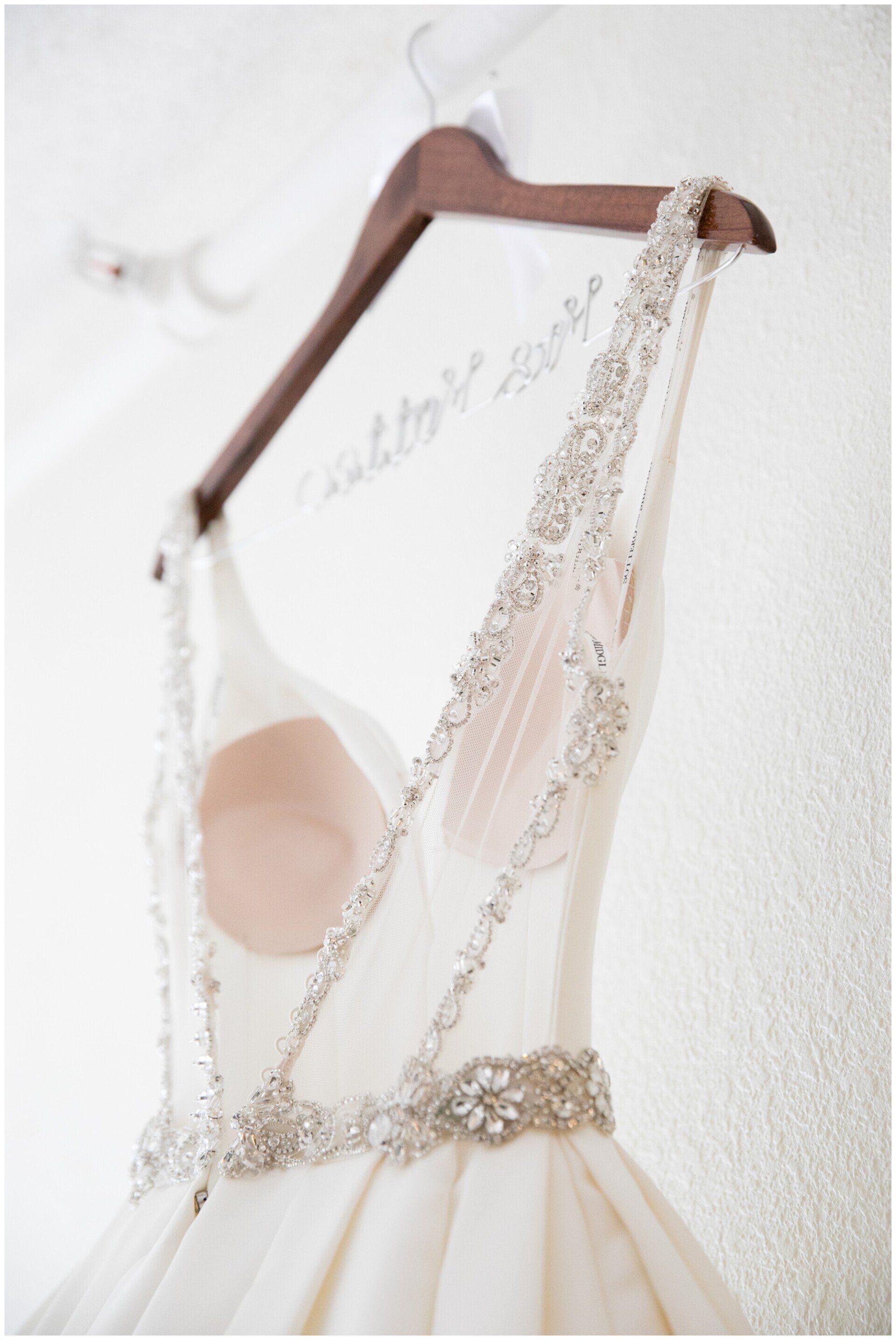Ivory lace dress on a wooden hanger against a white wall