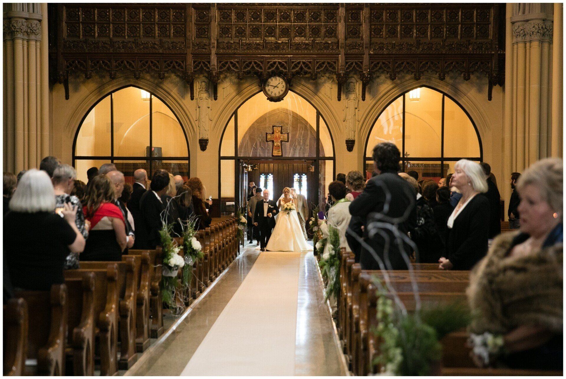 Wedding ceremony in a church aisle, with guests seated on both sides and a couple at the altar.