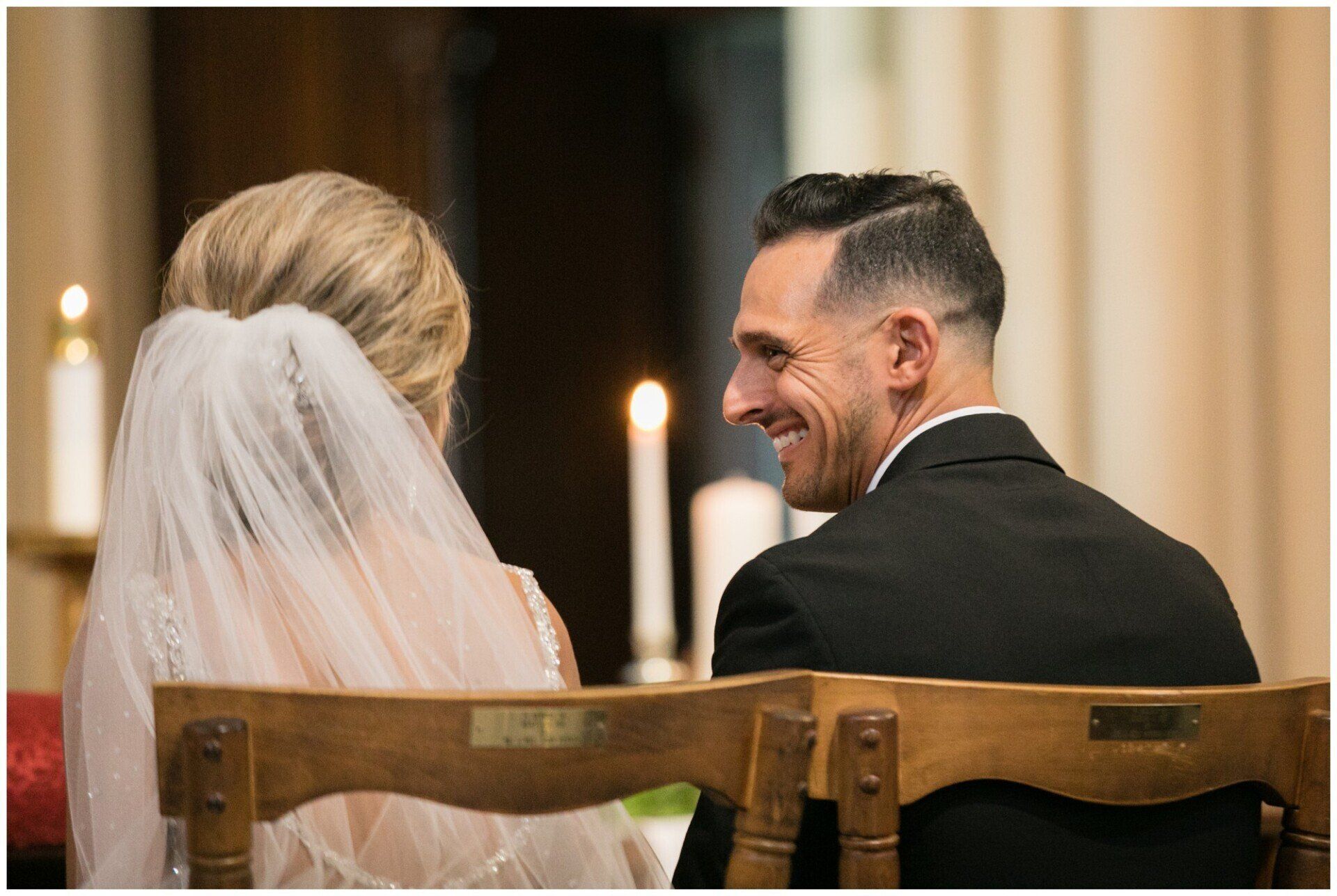 Bride and groom seated at a wedding ceremony, smiling at each other by candlelight