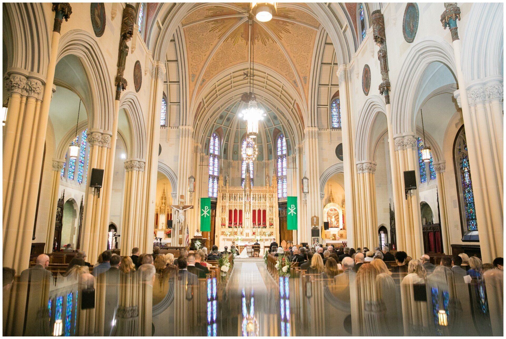 Grand cathedral interior with vaulted arches, stained glass, and people seated along the aisles